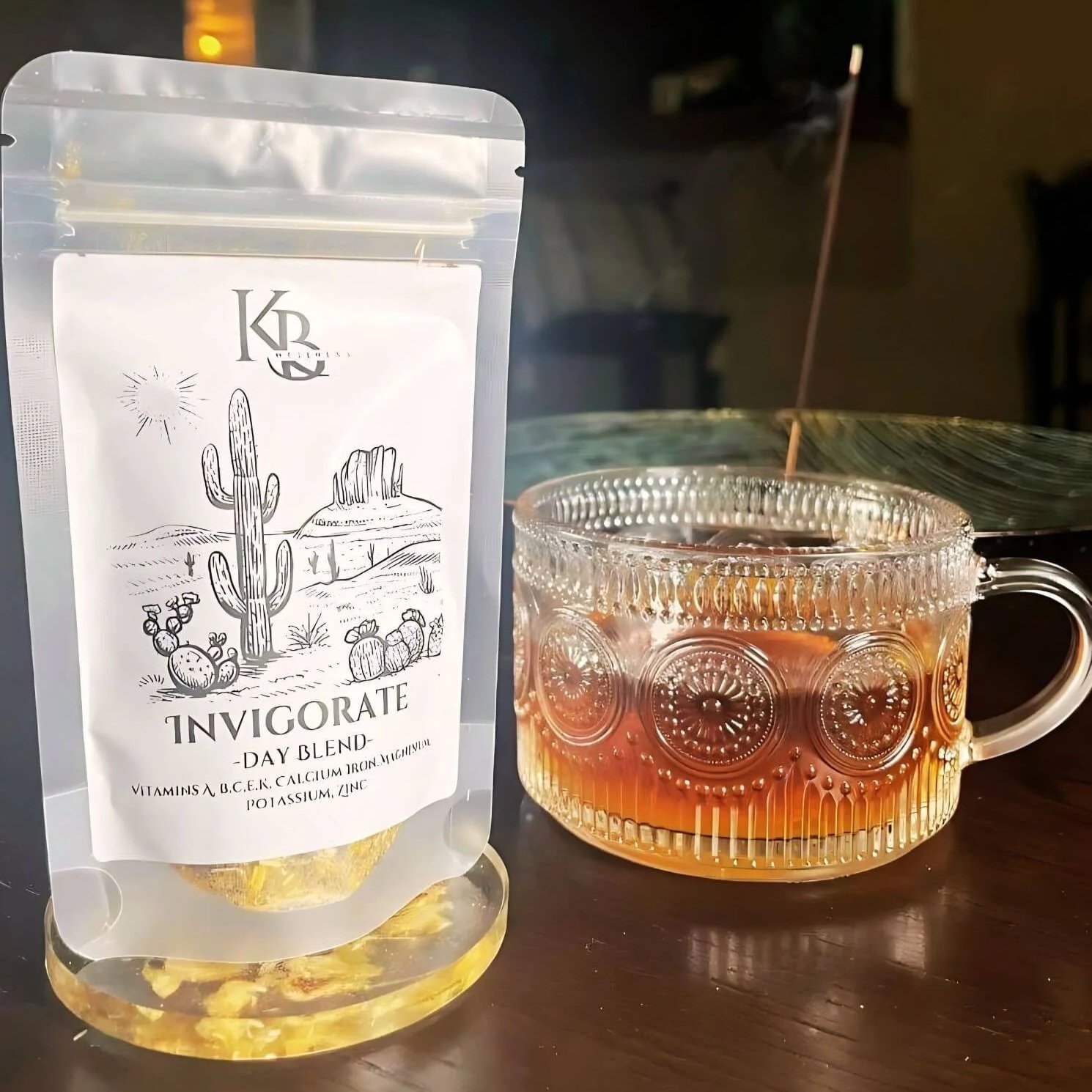 Invigorate herbal tea in it's pouch sitting besides a cup of brewed tea on a dark wooden table.