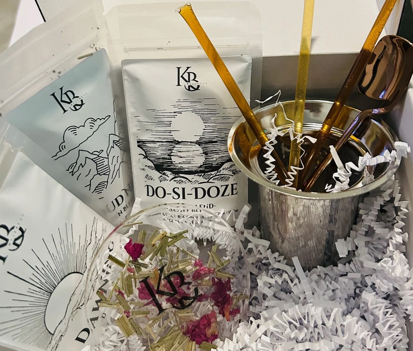 Various packages of tea labeled 'Do-Si-Doze' with a sun and mountain illustration, a metal container with tea stirrers and sunglasses, and shredded paper for packaging.