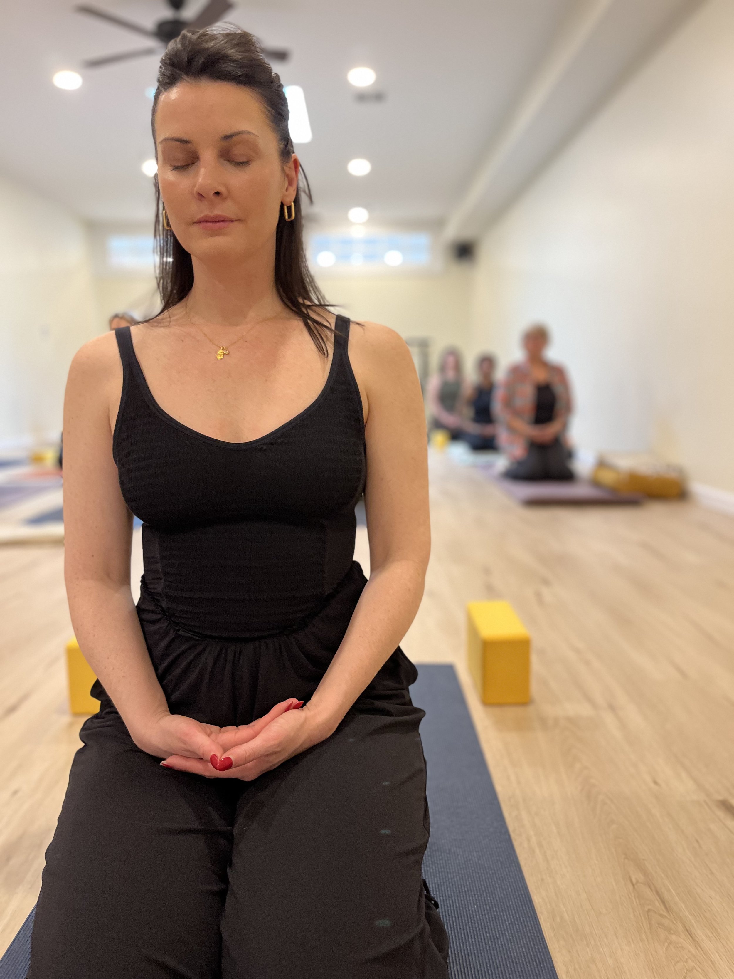 A woman in black romper seated quietly in meditation