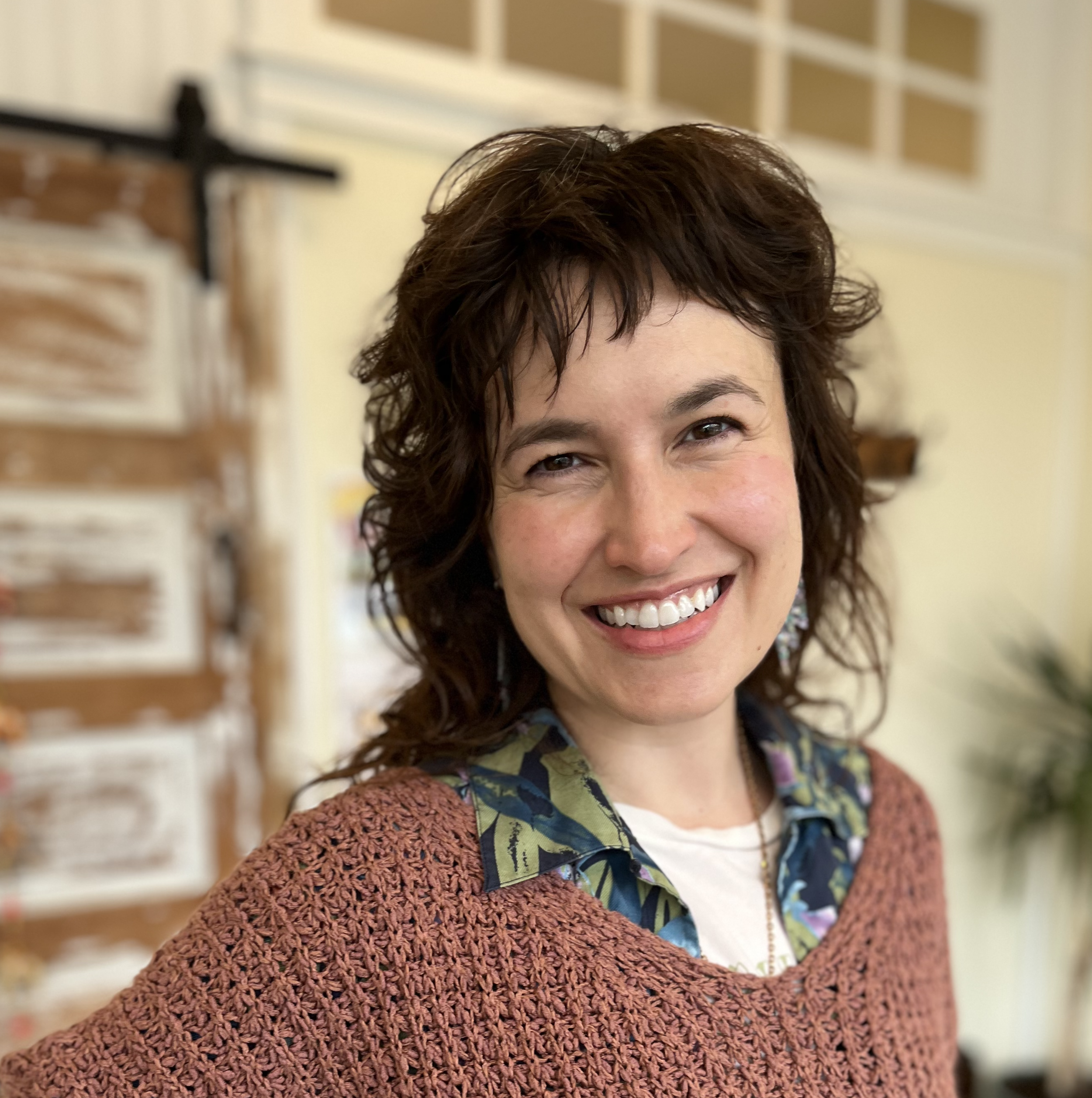 A woman with curly dark hair standing in front of a barn door inside a yoga studio.
