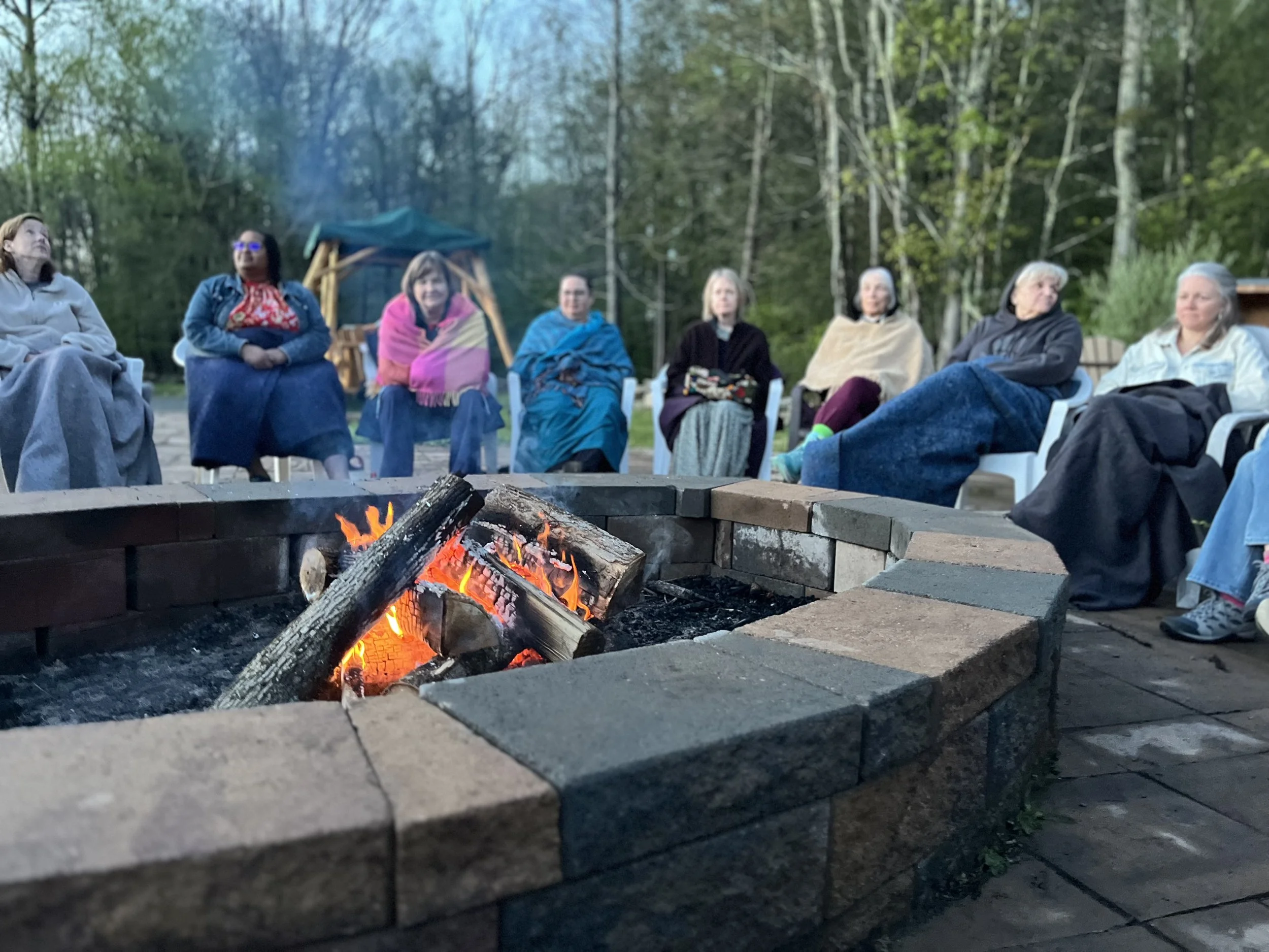 Women of all ages sitting in a circle around a fire.