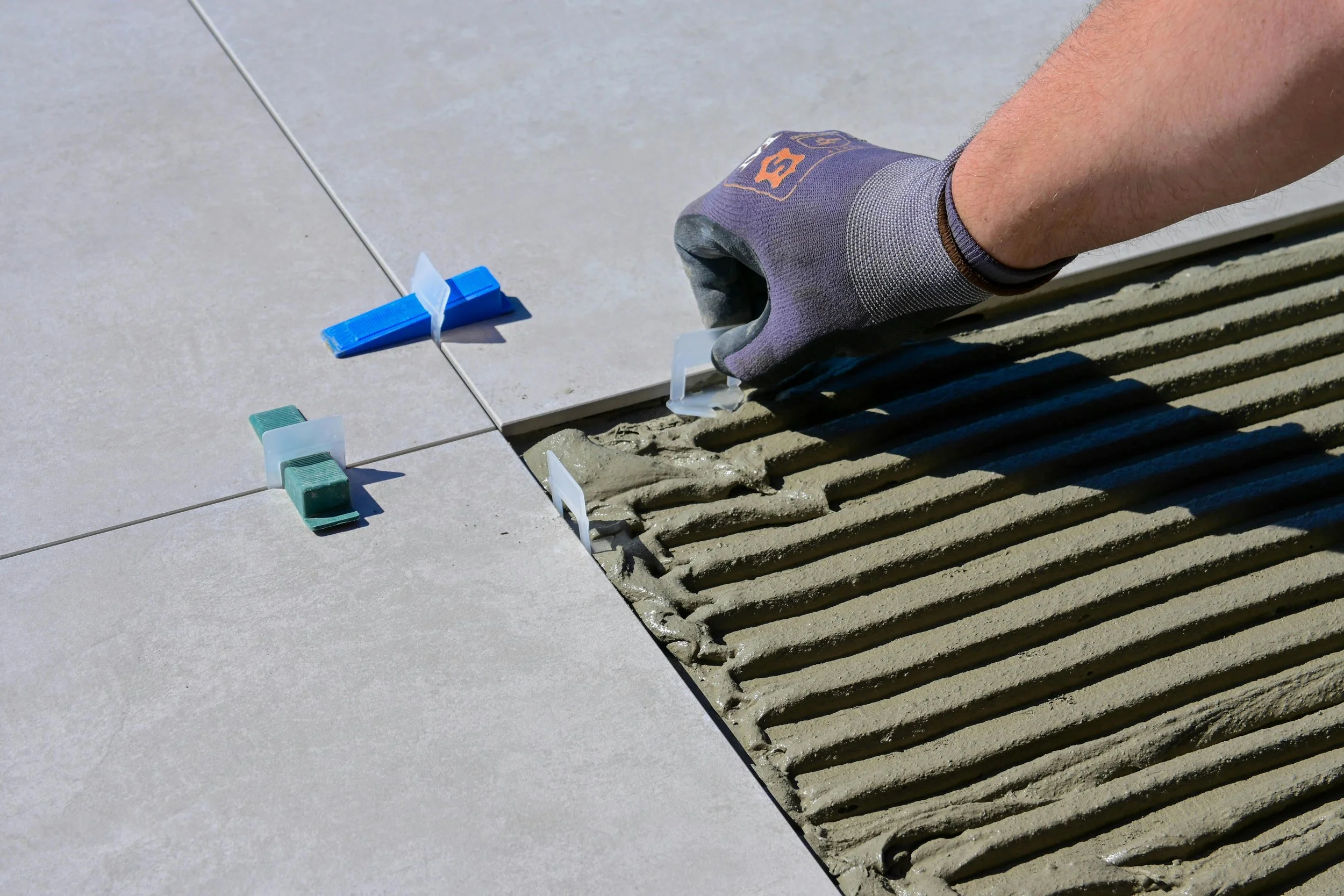 A person wearing gloves applies grout between tiles on a floor.