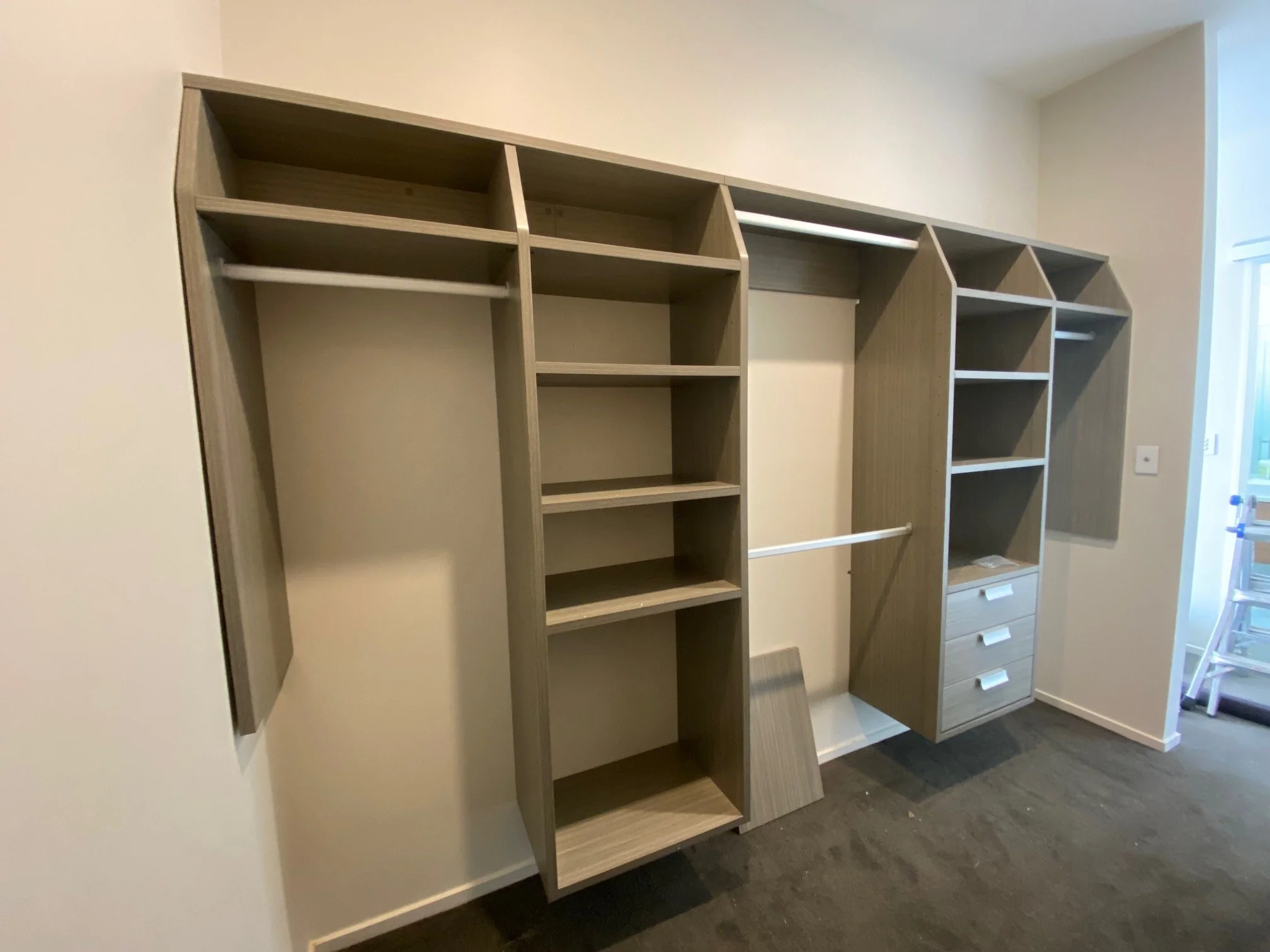 Empty custom built-in closet with shelves, drawers, and hanging rods in a room.