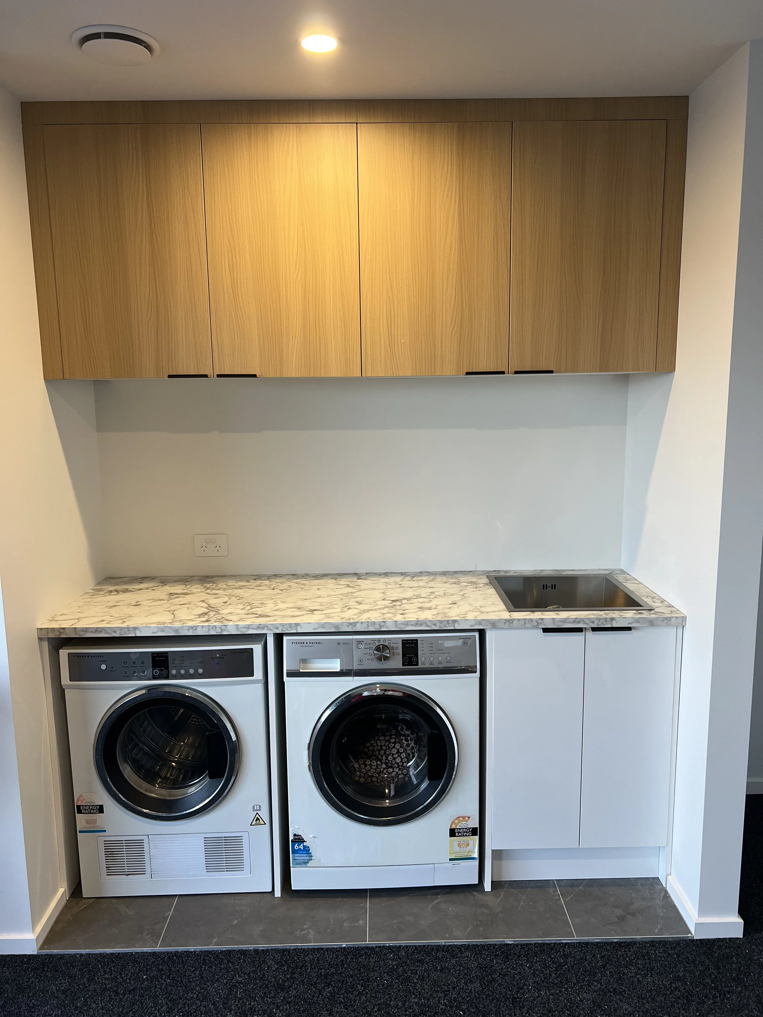 Laundry room with a marble countertop, a sink, and a washing machine and dryer below, with wooden cabinets above.