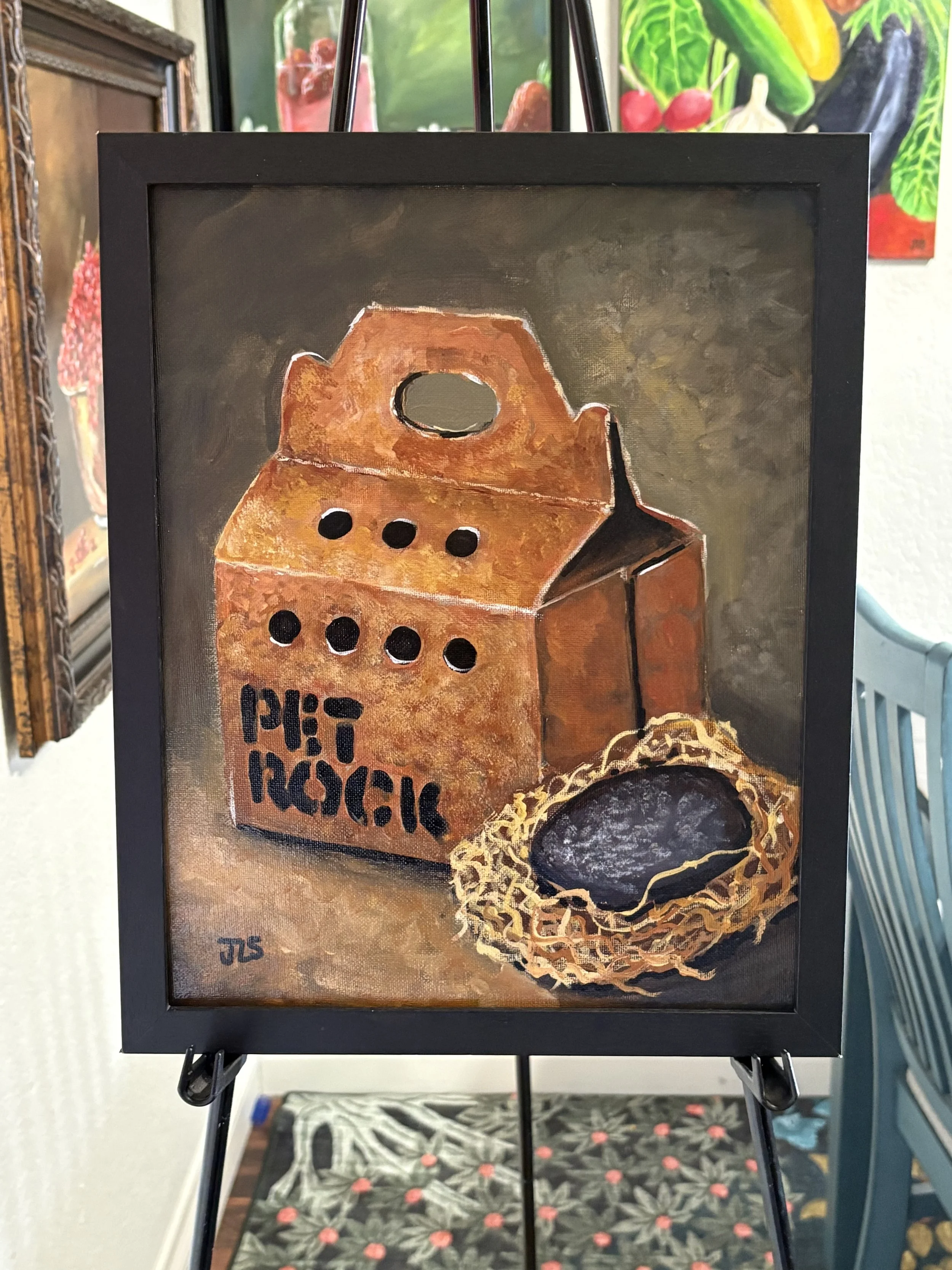 Cardboard pet carrier box labeled “PET ROCK” with air holes and a handle, with a gray rock resting on straw beside it