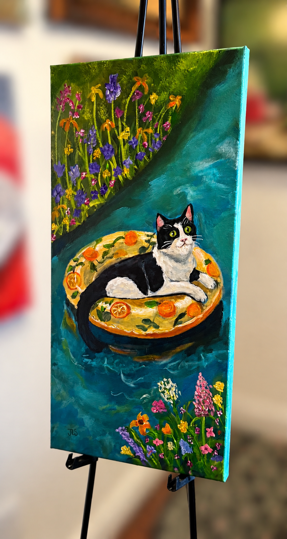 Tuxedo cat relaxing on an orange slice swim ring floating through a vibrant garden pond filled with pink, yellow, purple, and orange flowers
