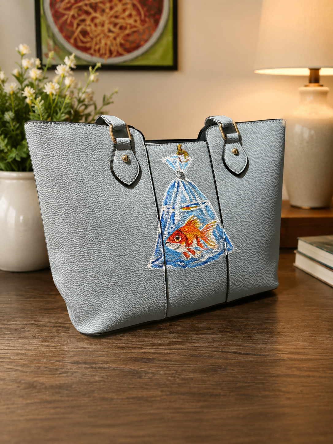Hand-painted blue shoulder handbag featuring a goldfish swimming inside a clear plastic bag.