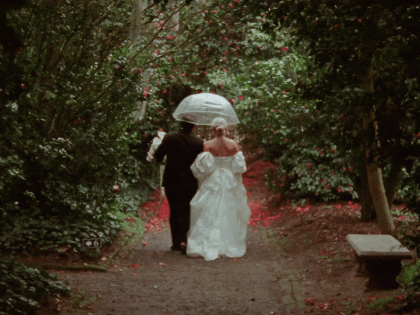Black and white photo of two people in wedding attire lying on grass.