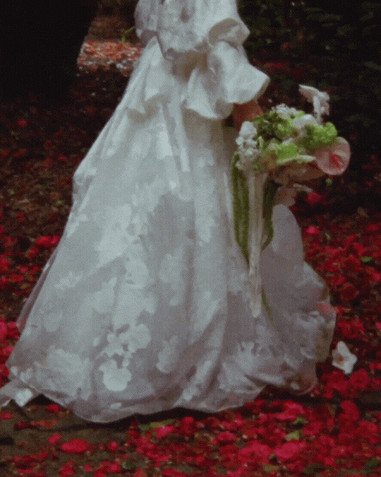 Black and white photo of two people in wedding attire lying on grass.