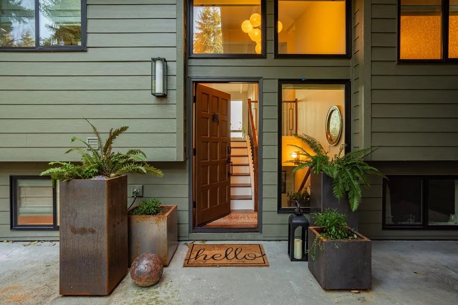 Front entry exterior of a Gig Harbor home remodel completed by a remodeling contractor, featuring new siding, modern windows, and contemporary planters.