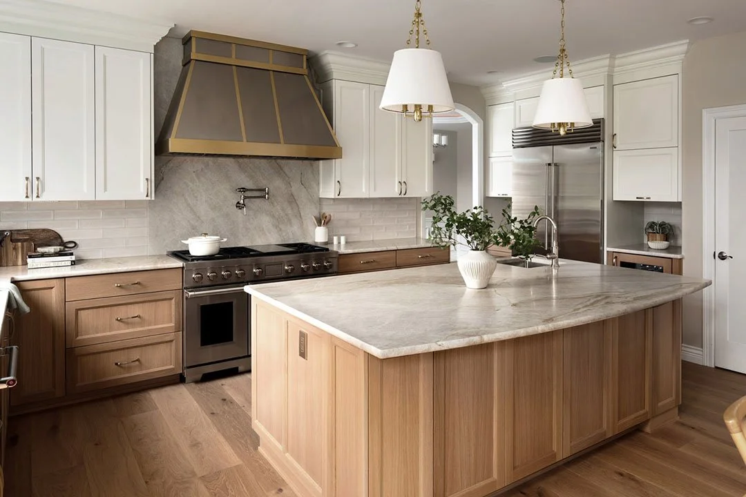 Award-winning Auburn kitchen remodel with custom white and natural wood cabinetry, quartz waterfall island, brass range hood, luxury appliances, and open-concept design by a Tacoma-area design-build remodeling contractor.