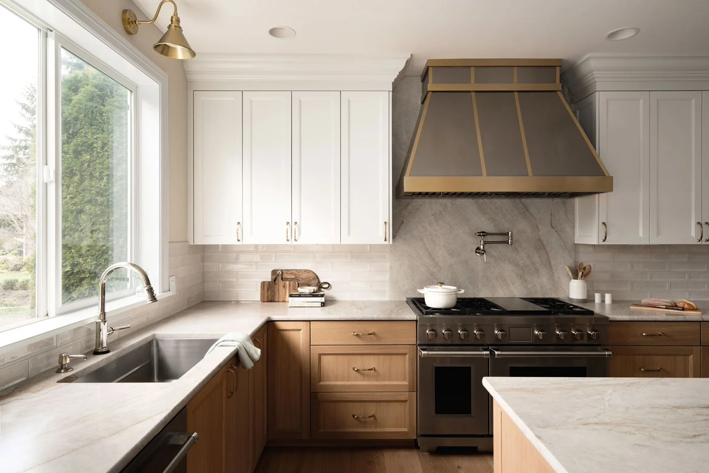 Tacoma kitchen remodel with white upper cabinets, warm wood cabinetry, marble backsplash, and custom brass range hood design