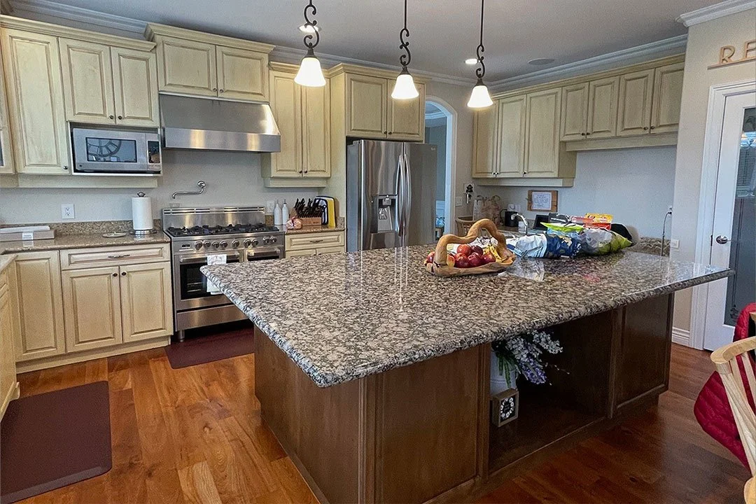 Before kitchen remodel in Auburn, WA featuring raised-panel cream cabinets, granite countertops, stainless steel appliances, and a large island prior to renovation and design-build remodeling.