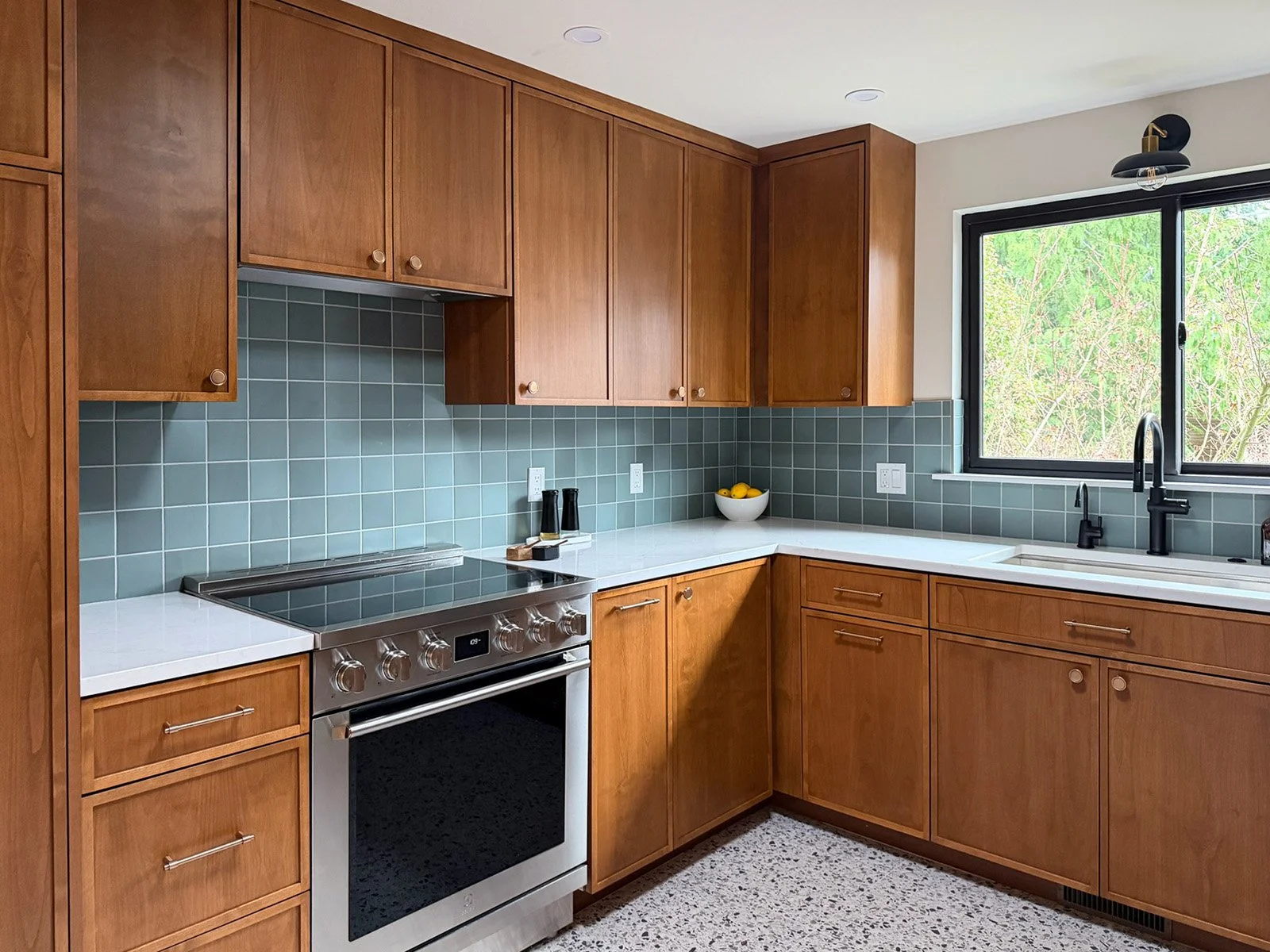 Warm Tacoma kitchen remodel featuring wood cabinetry, blue tile backsplash, white countertops, and large window bringing in natural light