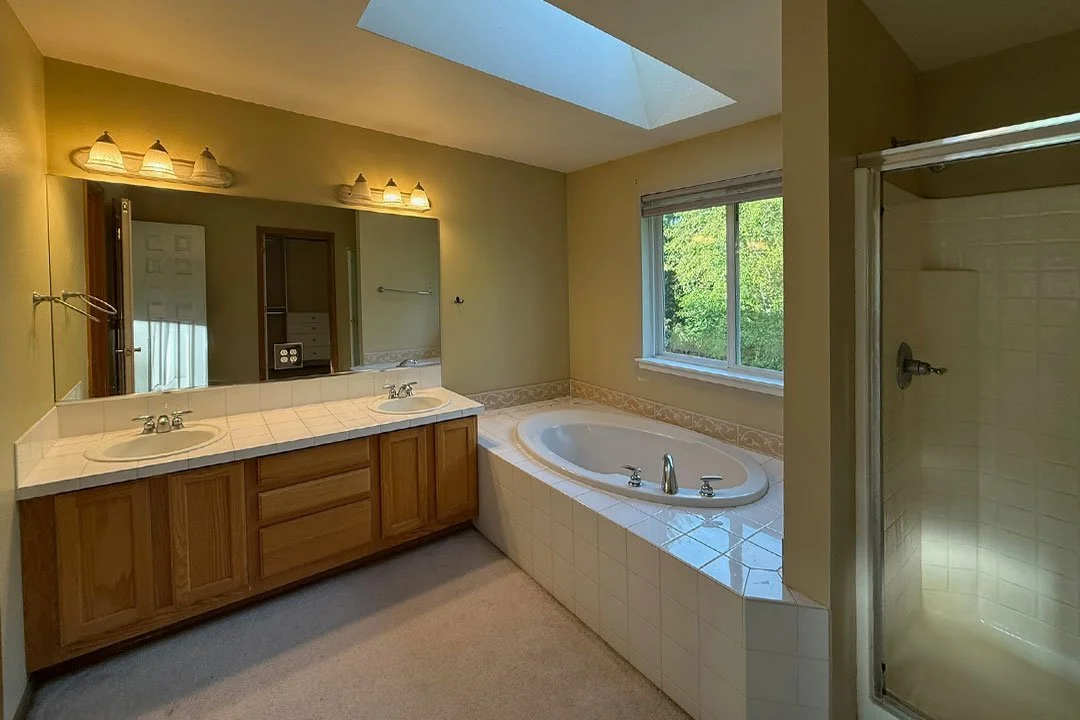 Before photo of a Puyallup primary bathroom remodel showing an outdated oak vanity, built-in soaking tub, carpet flooring, and traditional shower before renovation.
