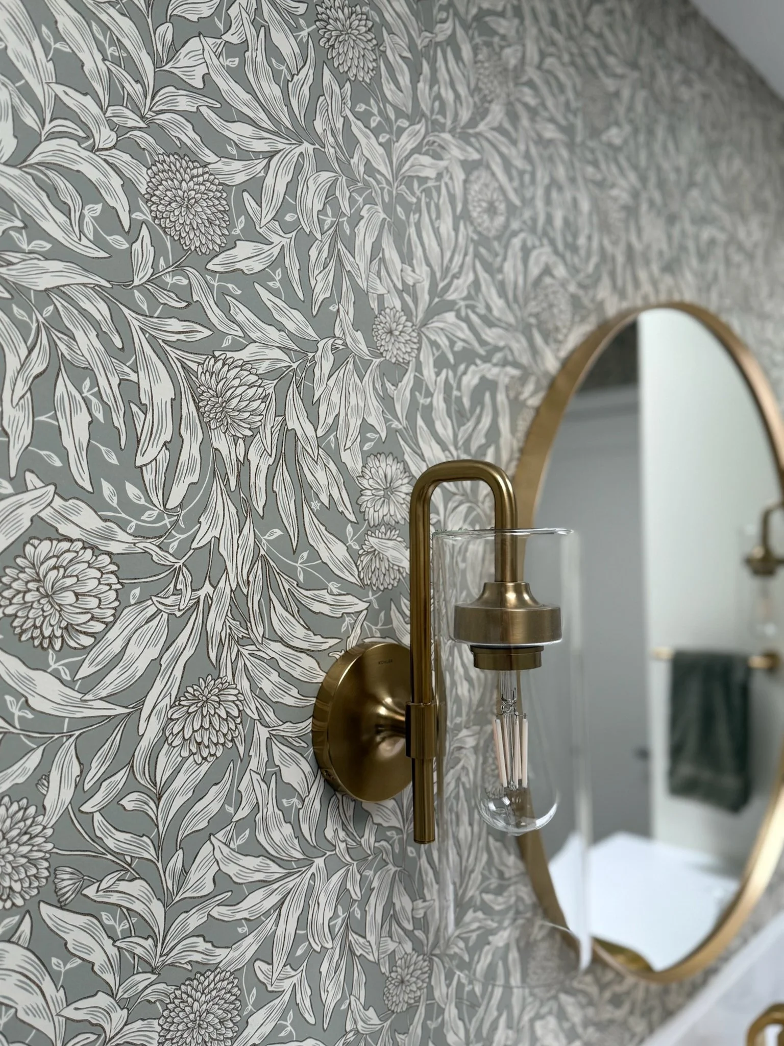 Detail view of the brushed brass wall sconce and sage floral wallpaper in a Gig Harbor powder room remodel completed by a remodeling contractor.