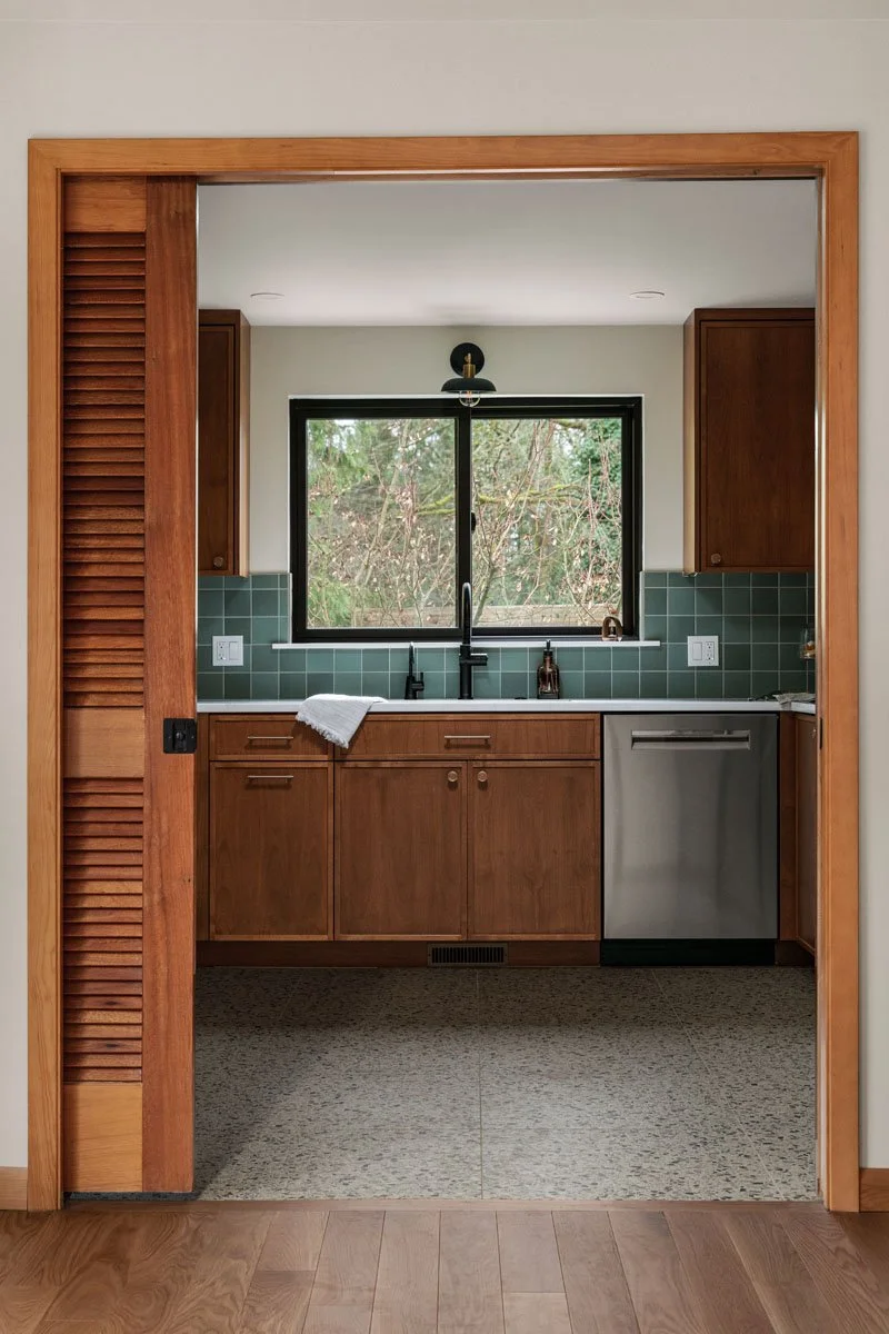 Sammamish WA kitchen remodel by a design-build remodeling contractor showing mid-century slatted pocket doors, custom wood cabinetry, green tile backsplash, and terrazzo flooring