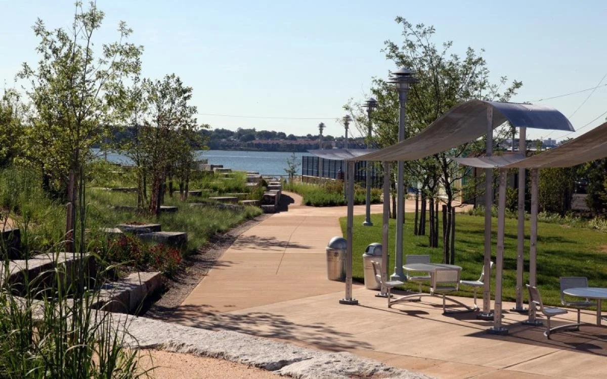 Water-adjacent park with native plants, shade structures, and stone seating