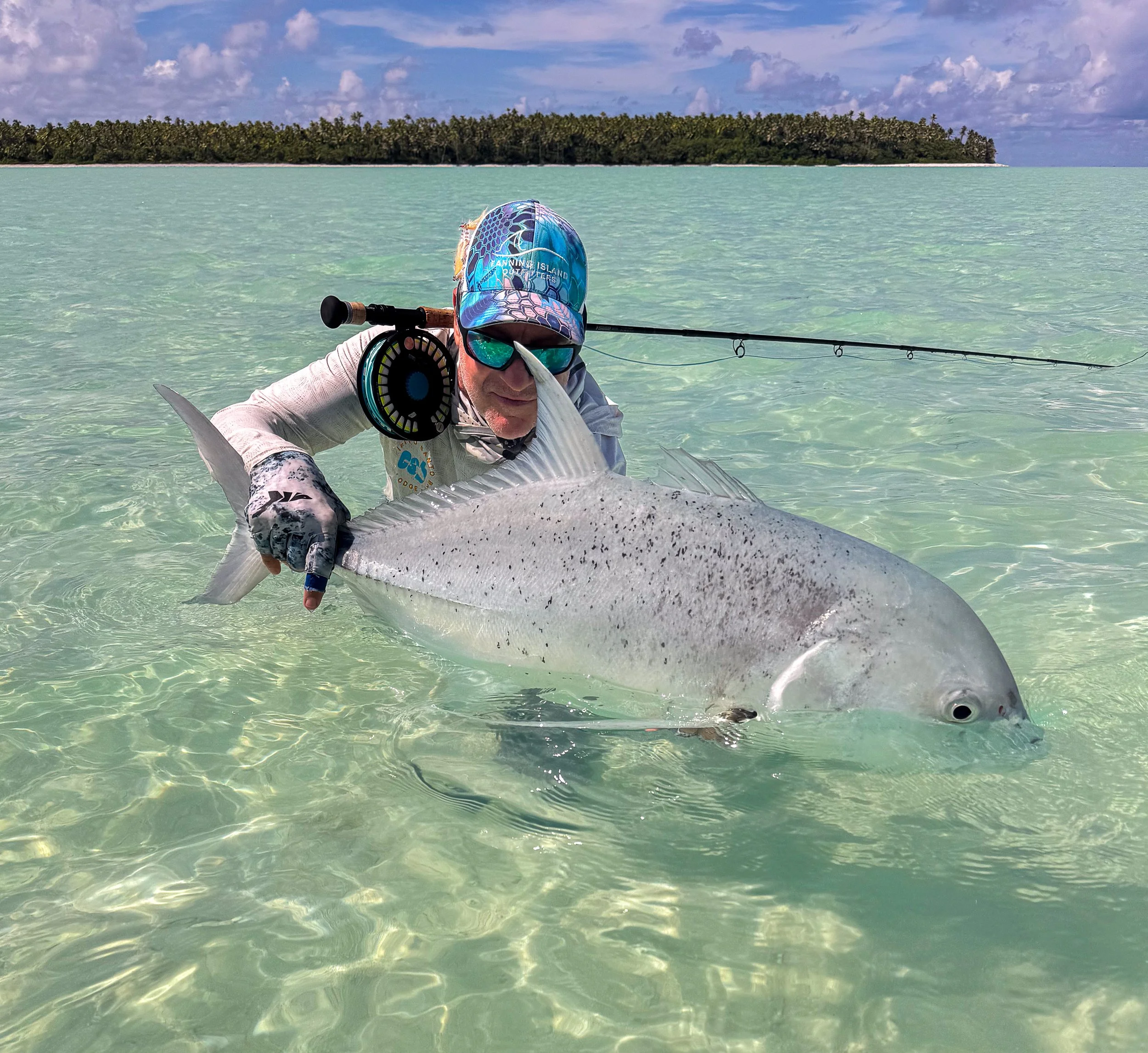 Saltwater anglers on Fanning Island with Giant Trevally and fly rod behind his head