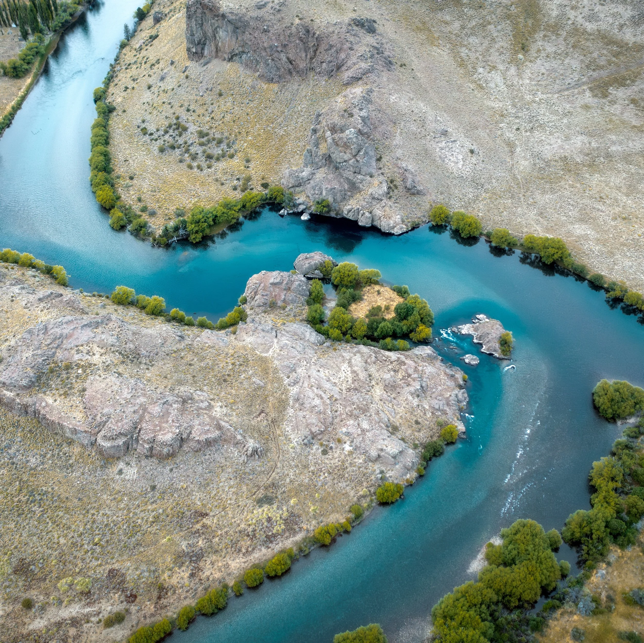 Aerial view of a winding river flowing through a canyon with steep, rocky cliffs and lush green trees along the riverbanks.