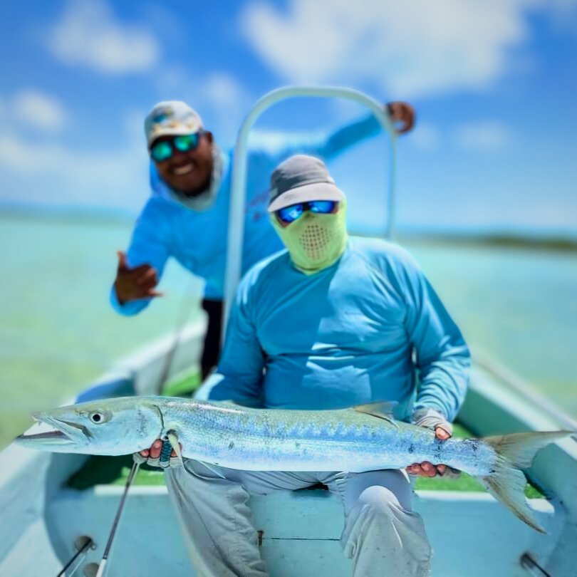 Angler on boat with barracuda and guide in background