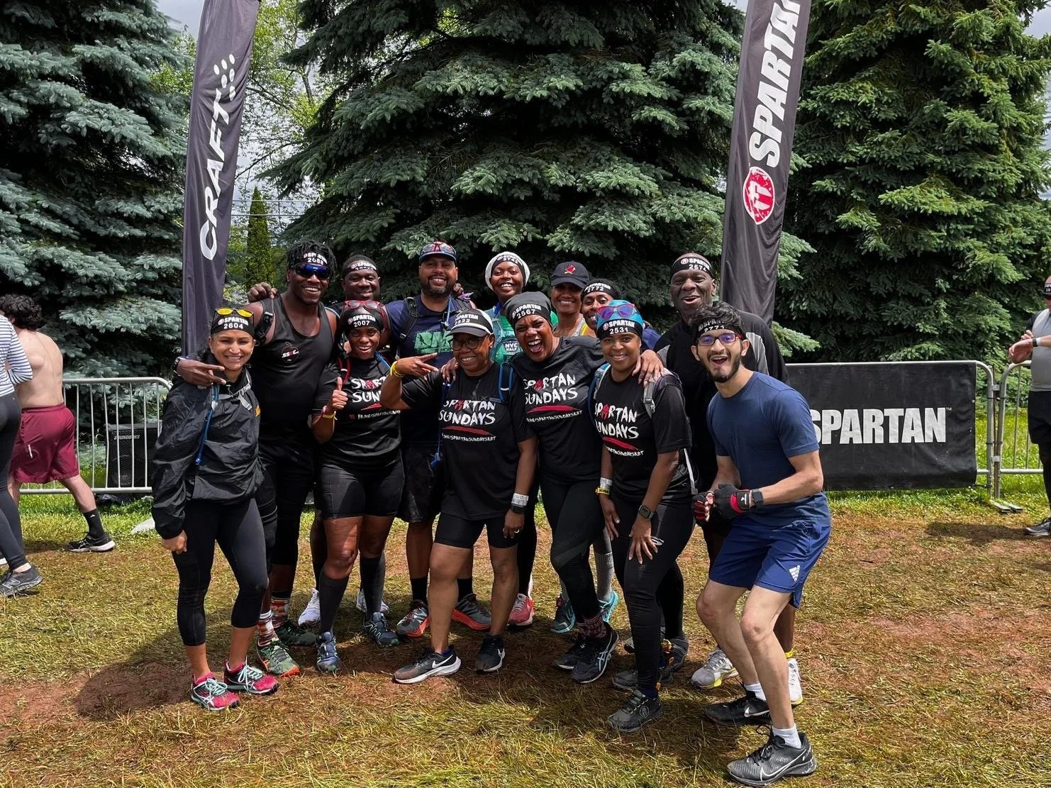 Group of people posing at a Spartan race event wearing athletic gear and headbands with trees in the background.
