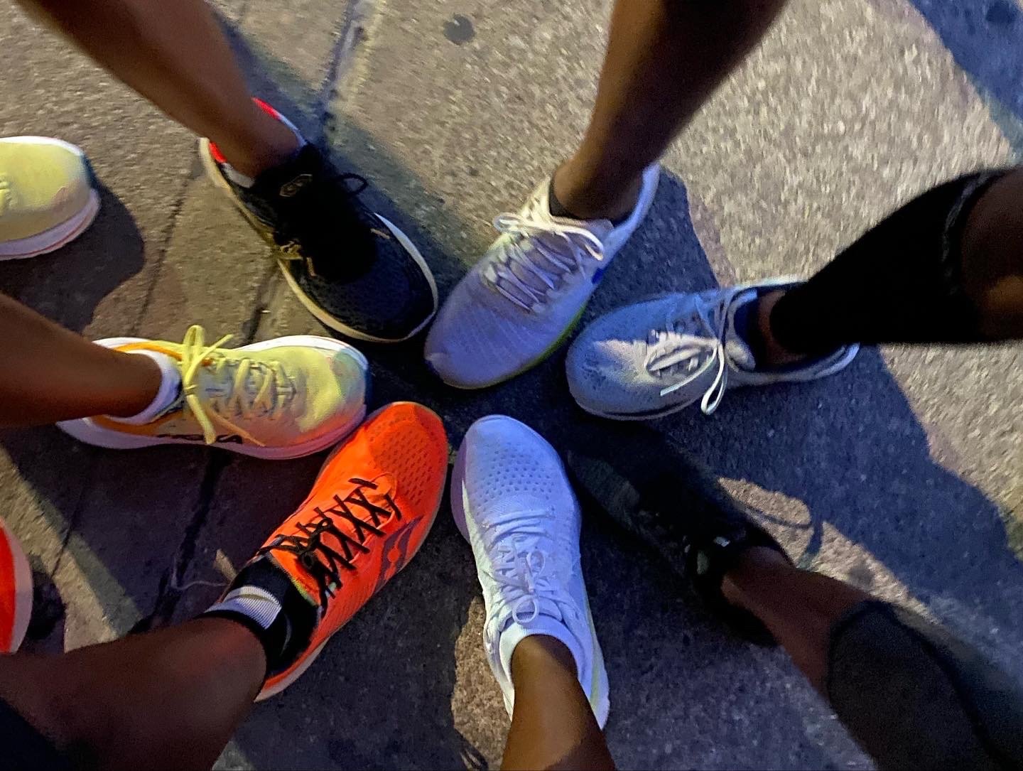 Group of people standing in a circle, showing various colorful running shoes on a concrete surface.