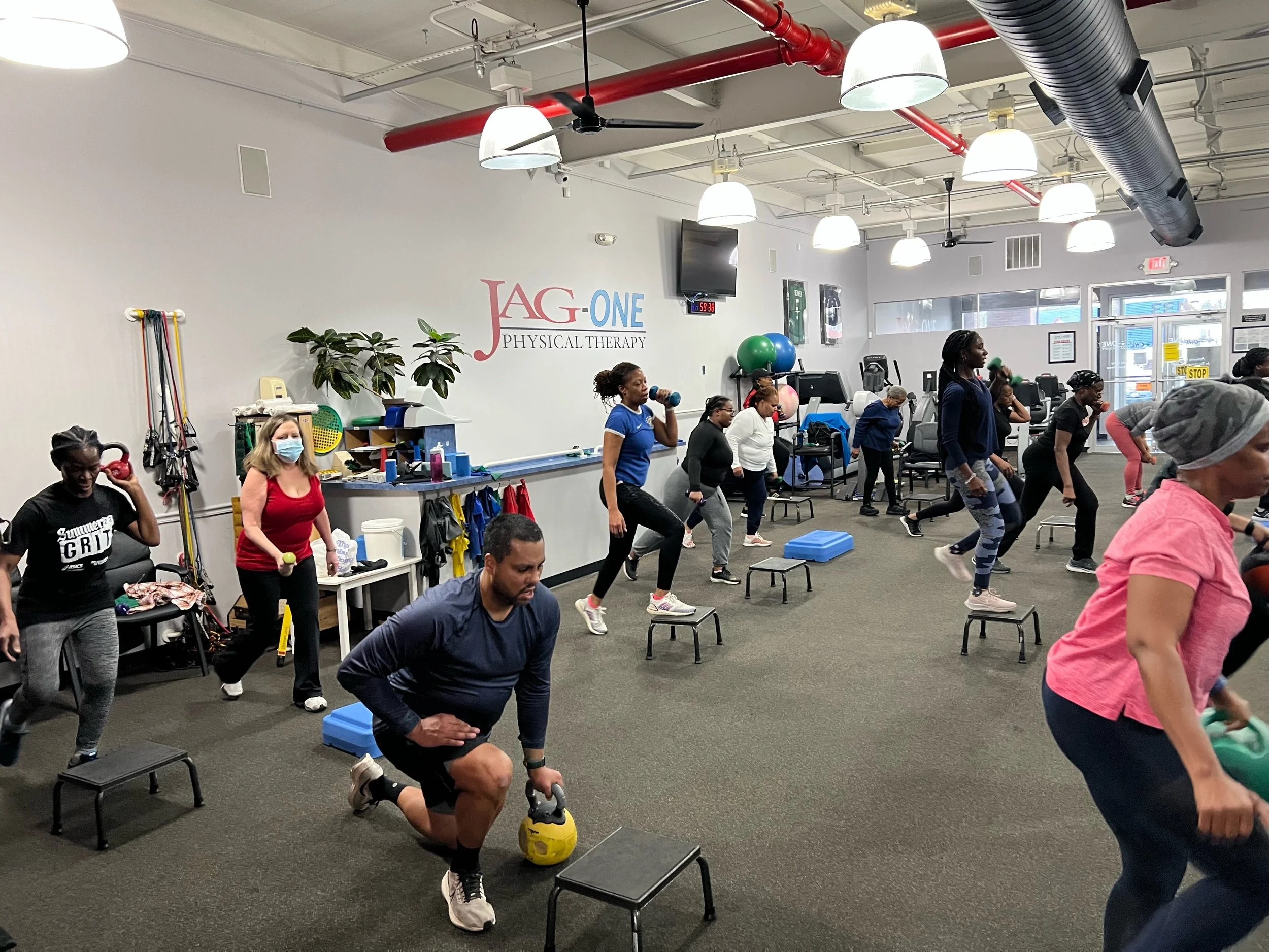 People exercising in a physical therapy clinic, using step platforms and kettlebells in a group workout session.