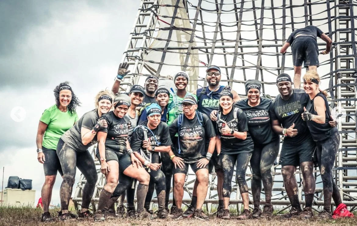 Spartans in front of a climbing obstacle at a Spartan race , muddy and smiling.