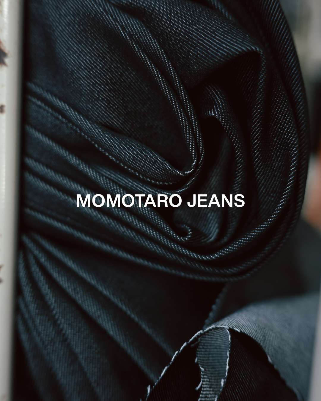 Close-up of stacked black denim jeans with white stitching, rolled up.
