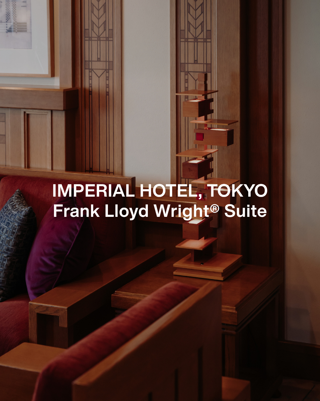 Interior of a hotel room with wooden furniture, a red upholstered bed with purple and patterned pillows, and a unique wooden sculpture on the bedside table.