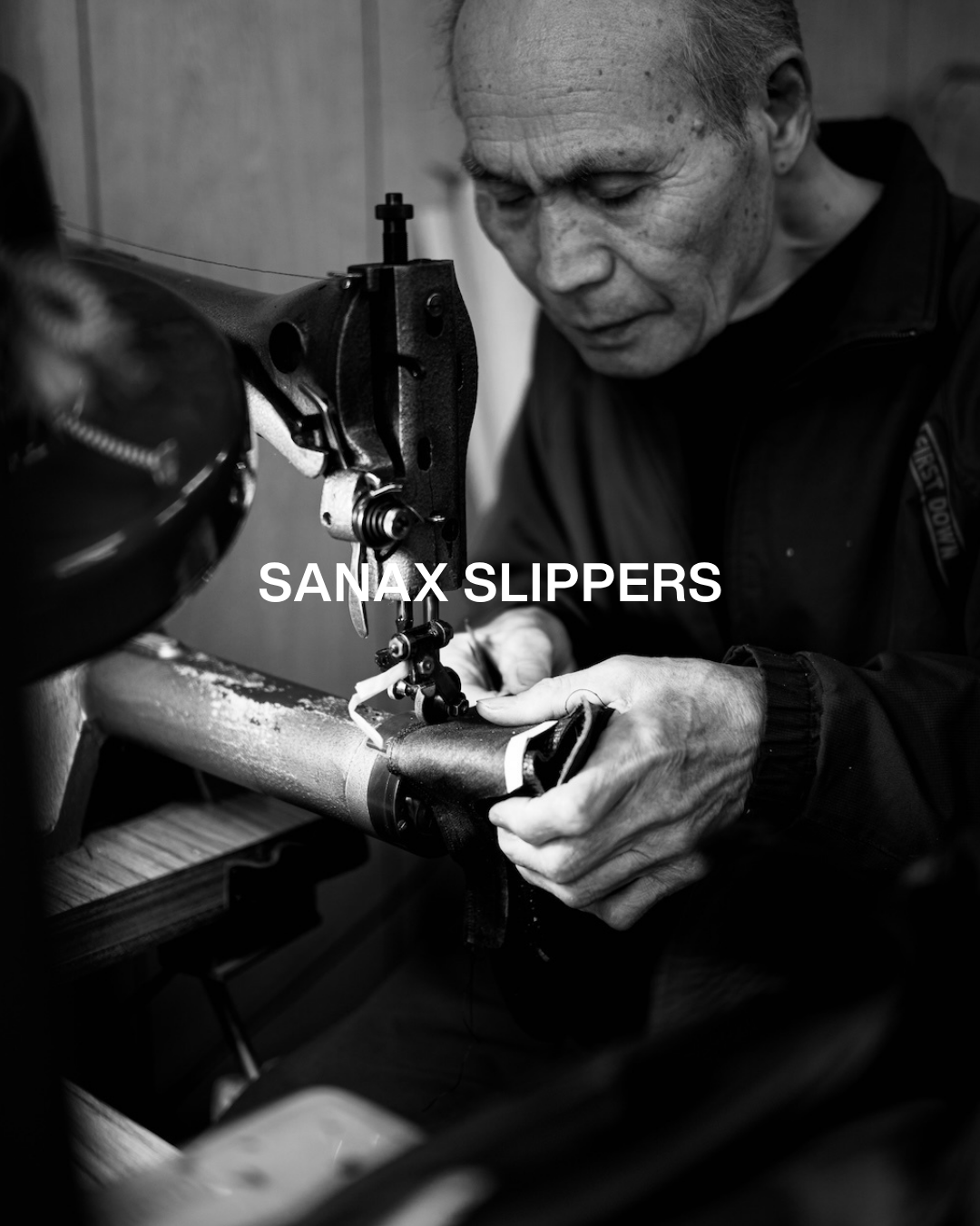Black and white photo of a man sewing a pair of black slippers on a sewing machine, with the text 'SANAX SLIPPERS' overlayed