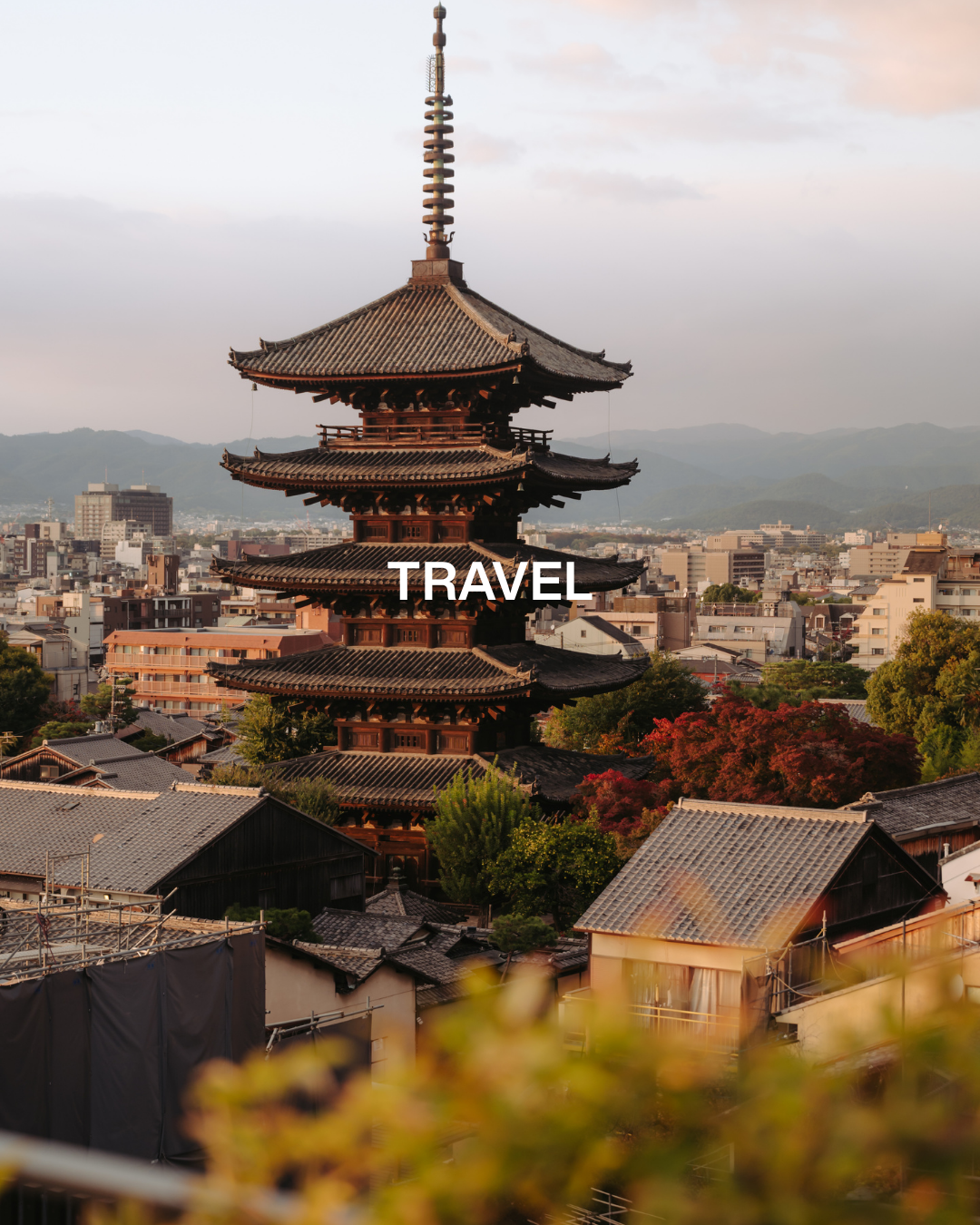 Traditional Japanese pagoda overlooking a cityscape with mountains in the background and autumn trees in the foreground.
