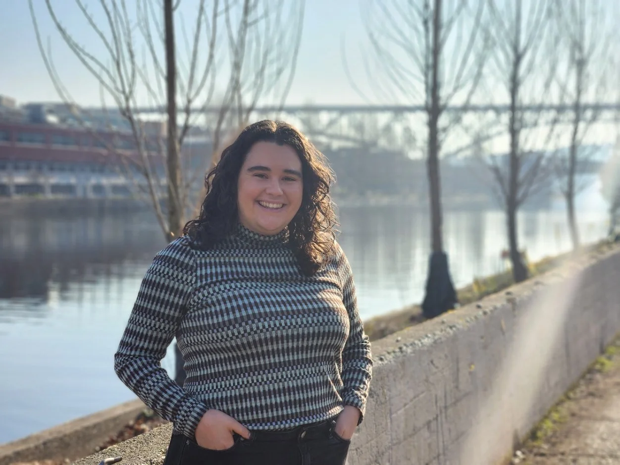 A Seattle therapist stands outside her Queen Anne office next to the Fremont canal. She has her hands in her pockets and is smiling at the camera.