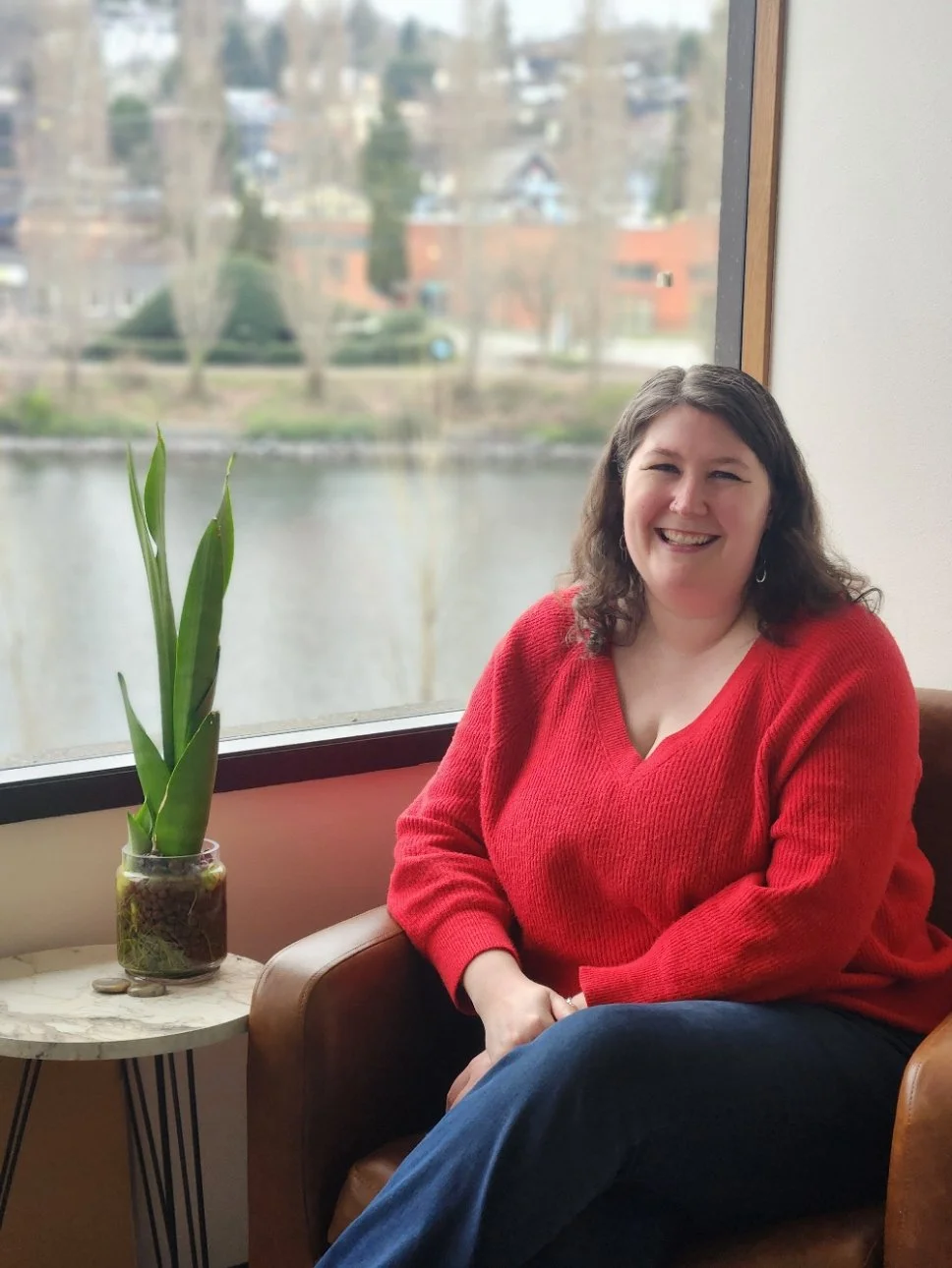 A seattle therapist who specializes in eating disorders and body image sits in her Queen Anne office, where there is a plant next to her and the canal out the window.