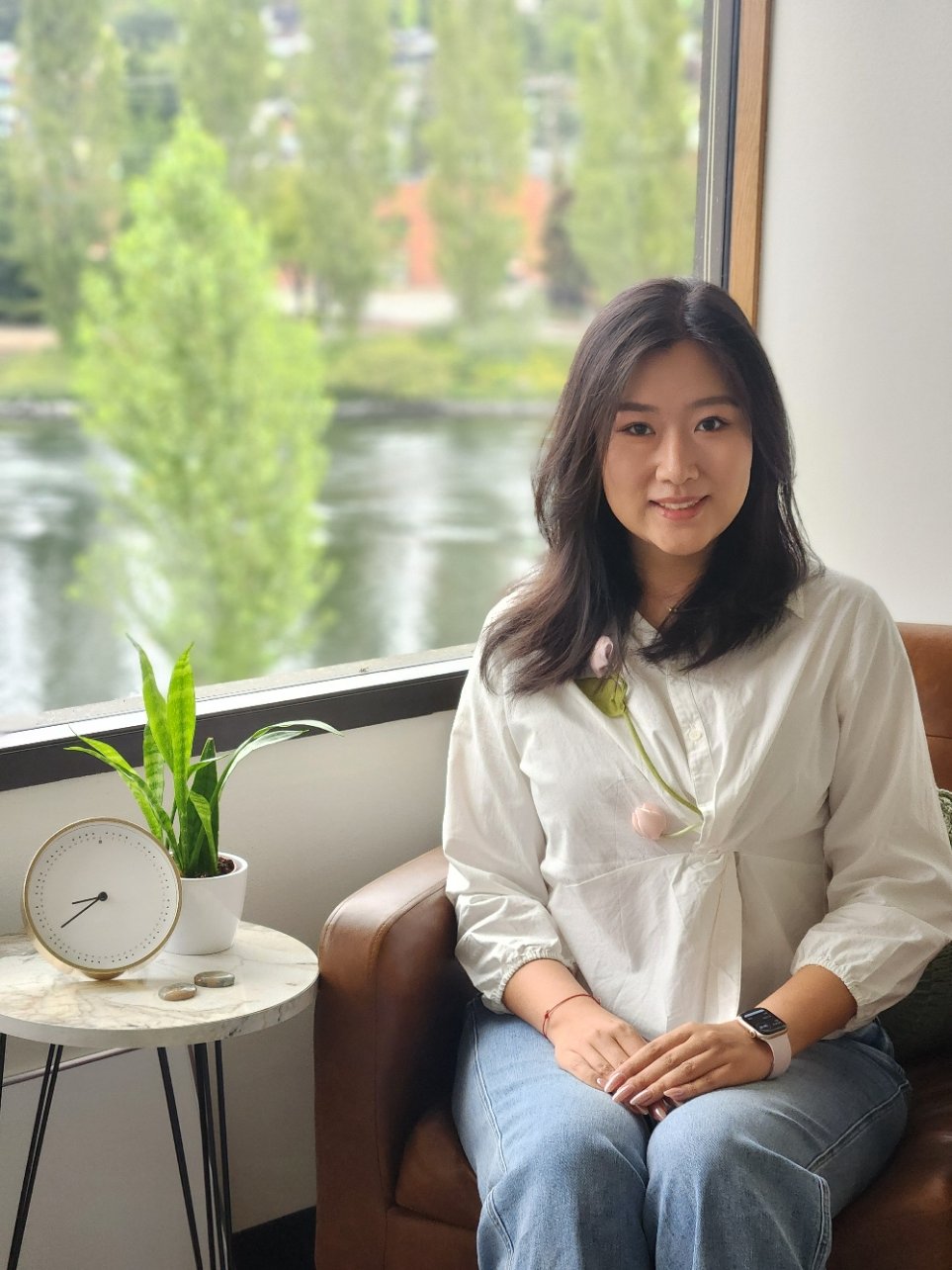 Seattle therapist Xinlei sits by a window with the Fremont canal outside. She supports clients with depression, anxiety, trauma, chronic illness, and immigration issues.