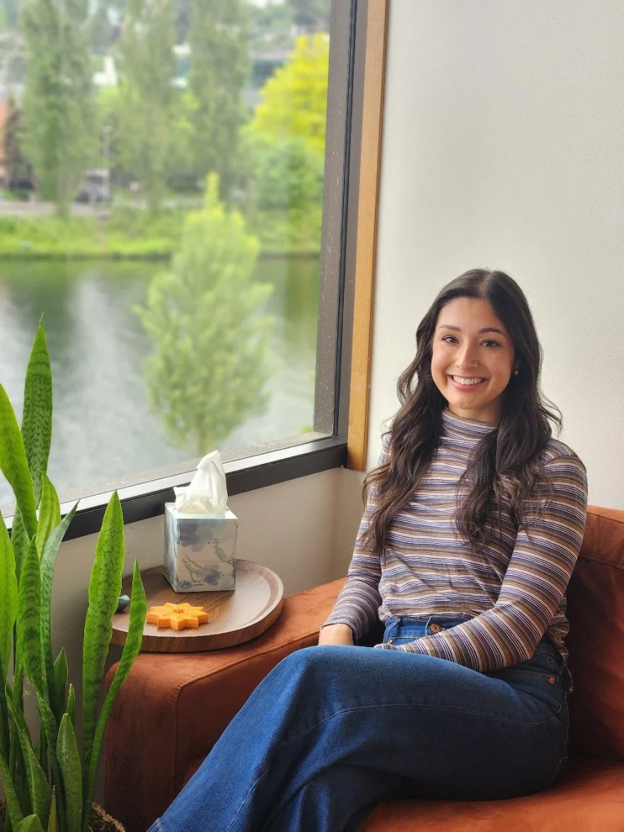 Seattle perfectionism, grief, and couples counselor sits on an orange couch with the Queen Anne canal visible outside the window.
