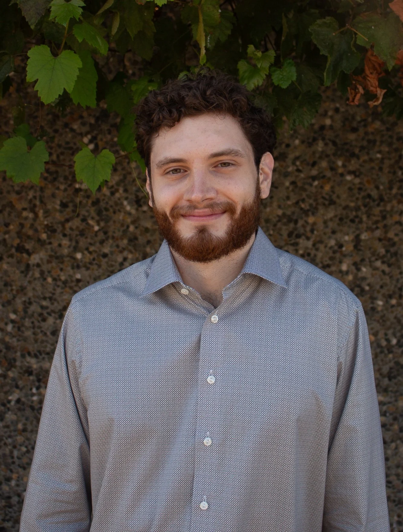 Matt, a mental health therapy graduate student who offers therapy at low cost in Seattle and virtually in Washington stands in front of a stone wall with green leaves on it.