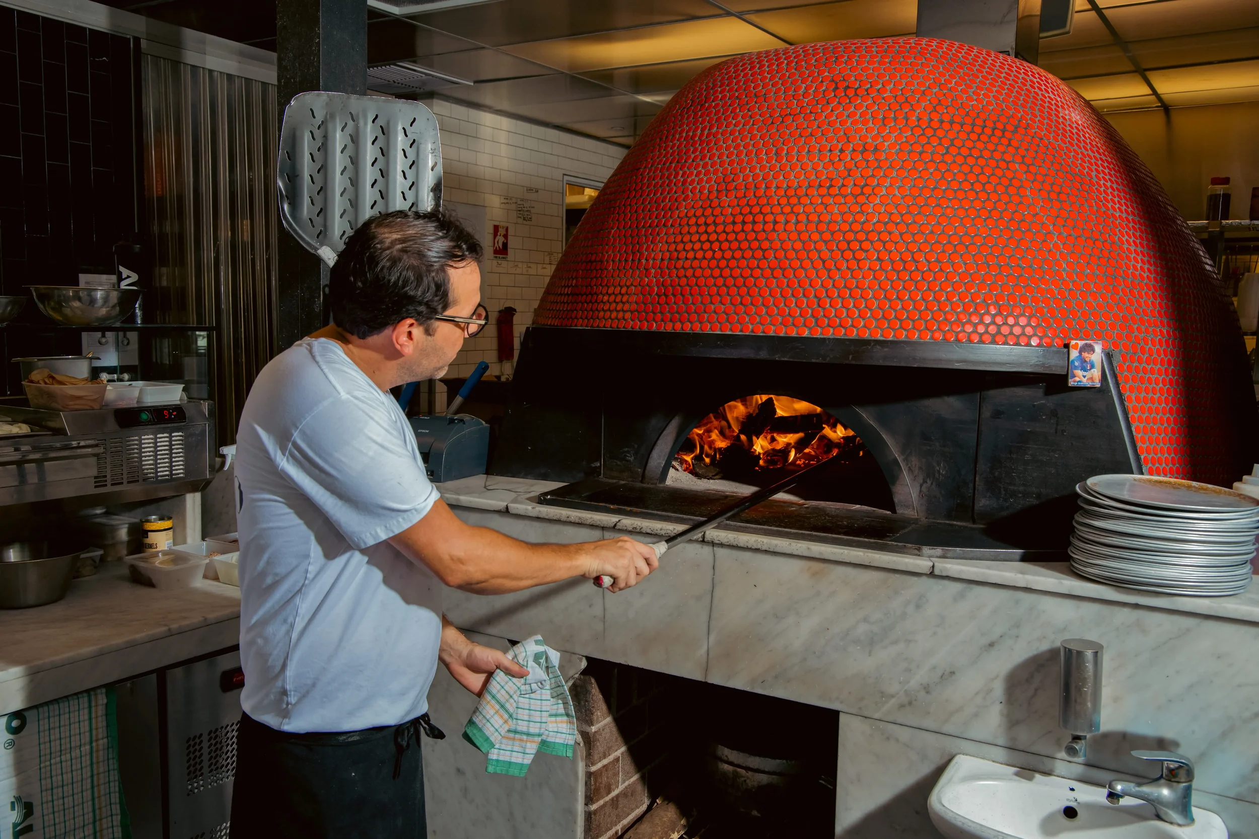 Chef sliding pizza into the wood fired oven at Da Mario Italian restaurant in Rosebery, Sydney