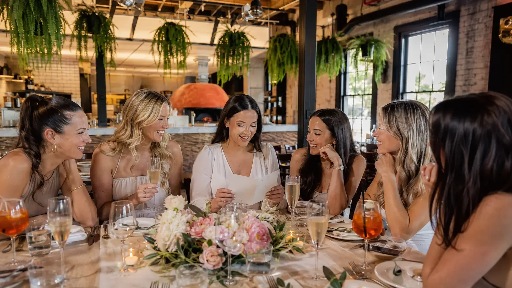 Bride opening a card at her bridal shower surrounded by friends with prosecco glasses on the table