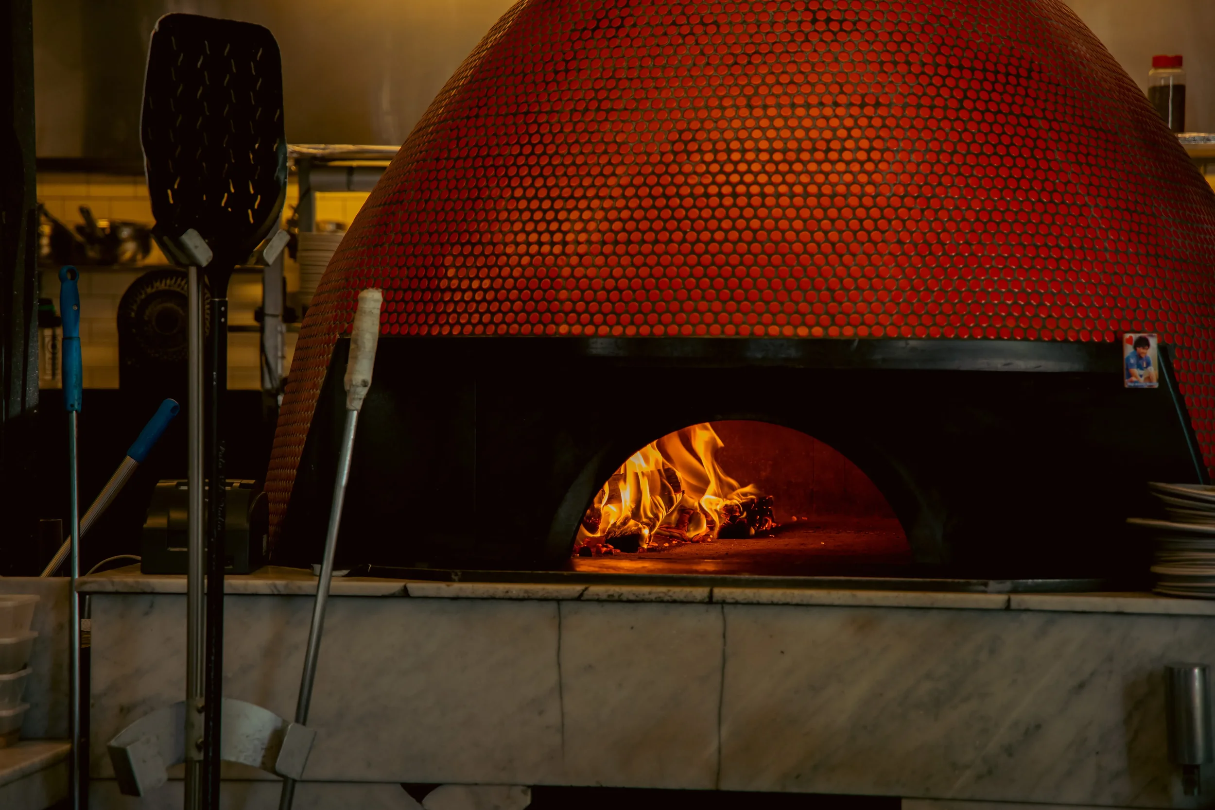 Interior of a traditional wood fired oven showing the brick dome, burning hardwood, and glowing stone floor