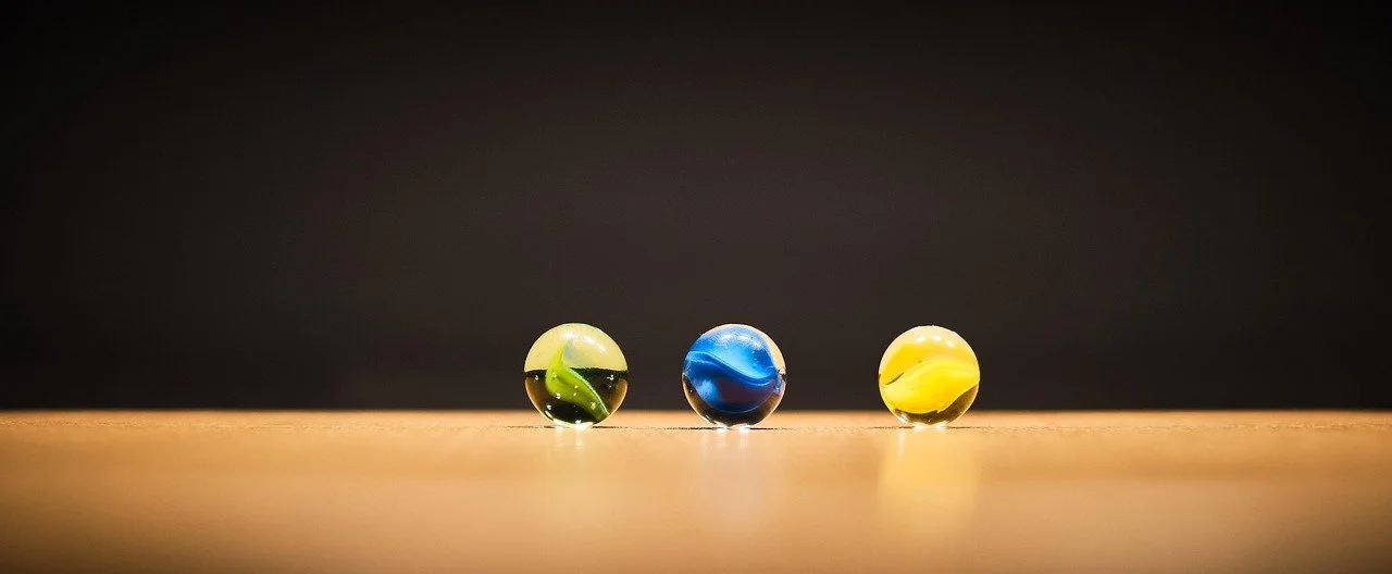 Three marbles in green, blue, and yellow colors on a wooden surface against a dark background.