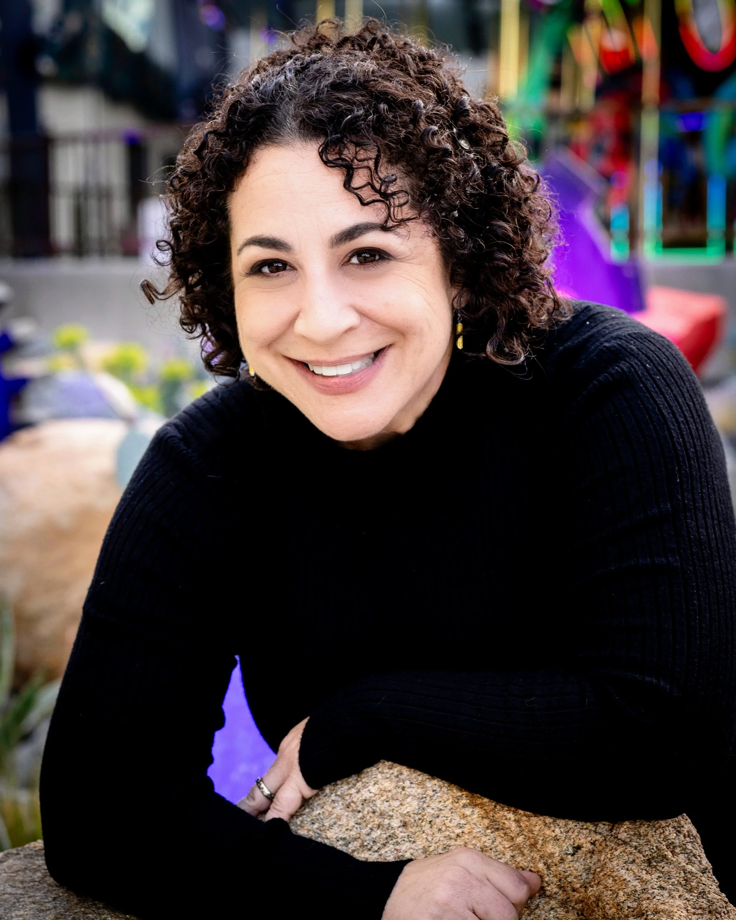 Aleza Freeman smiles at the camera, wearing a black sweater, with colorful decorations in the background.