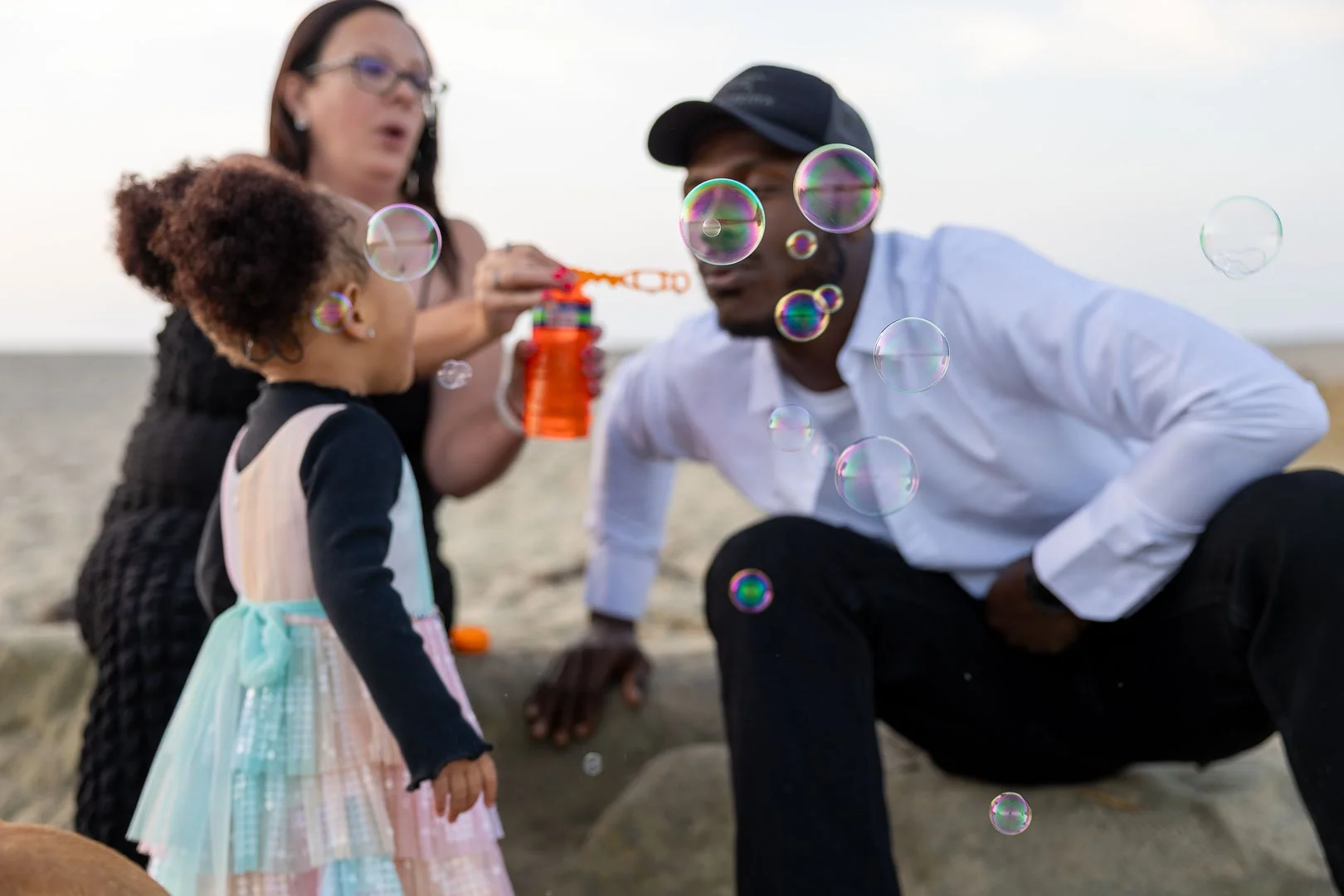 A family of three playing with bubbles on the beach during sunset.