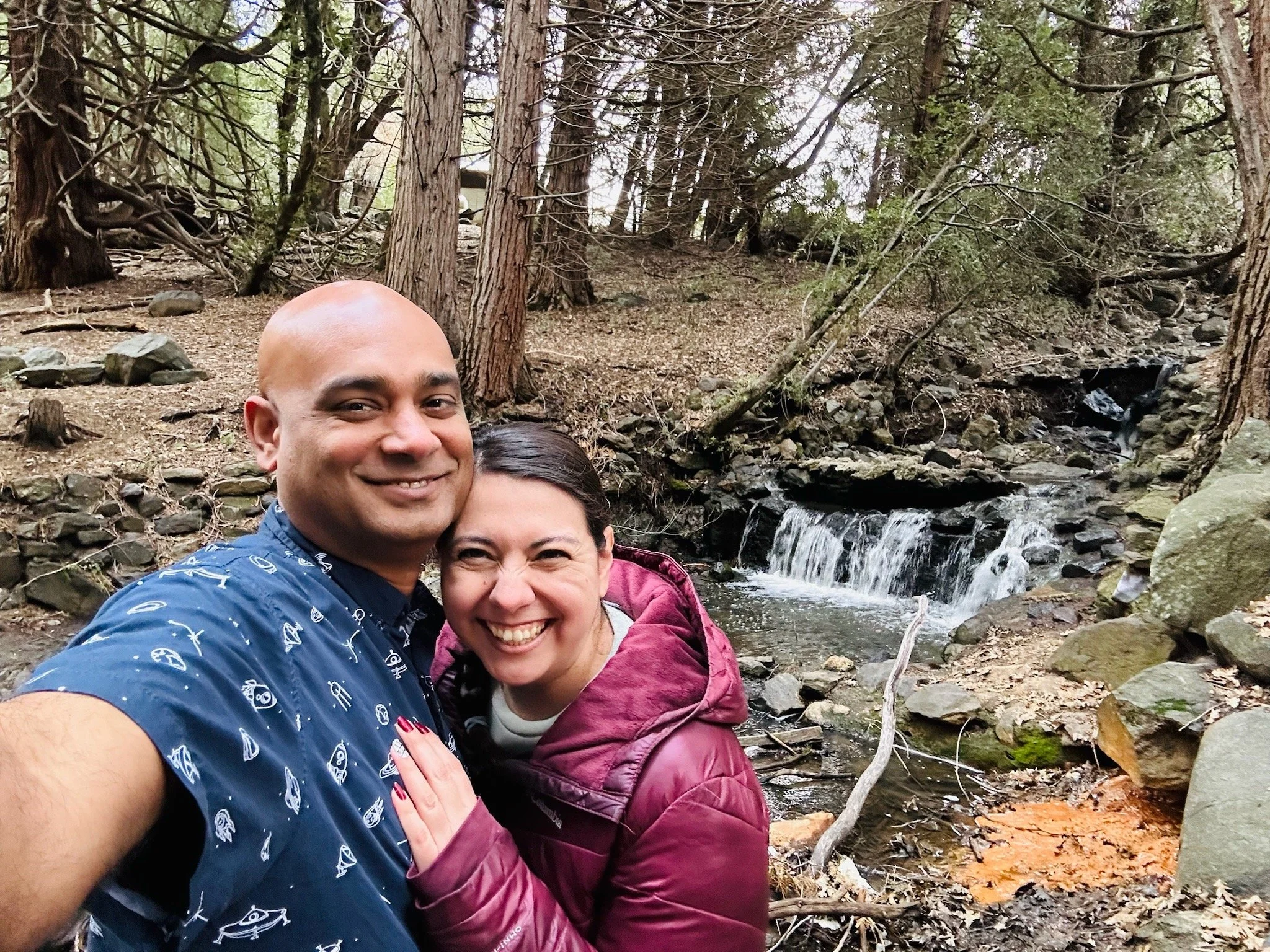 Ruwan and Diana taking a selfie in a forest near a small waterfall and stream.