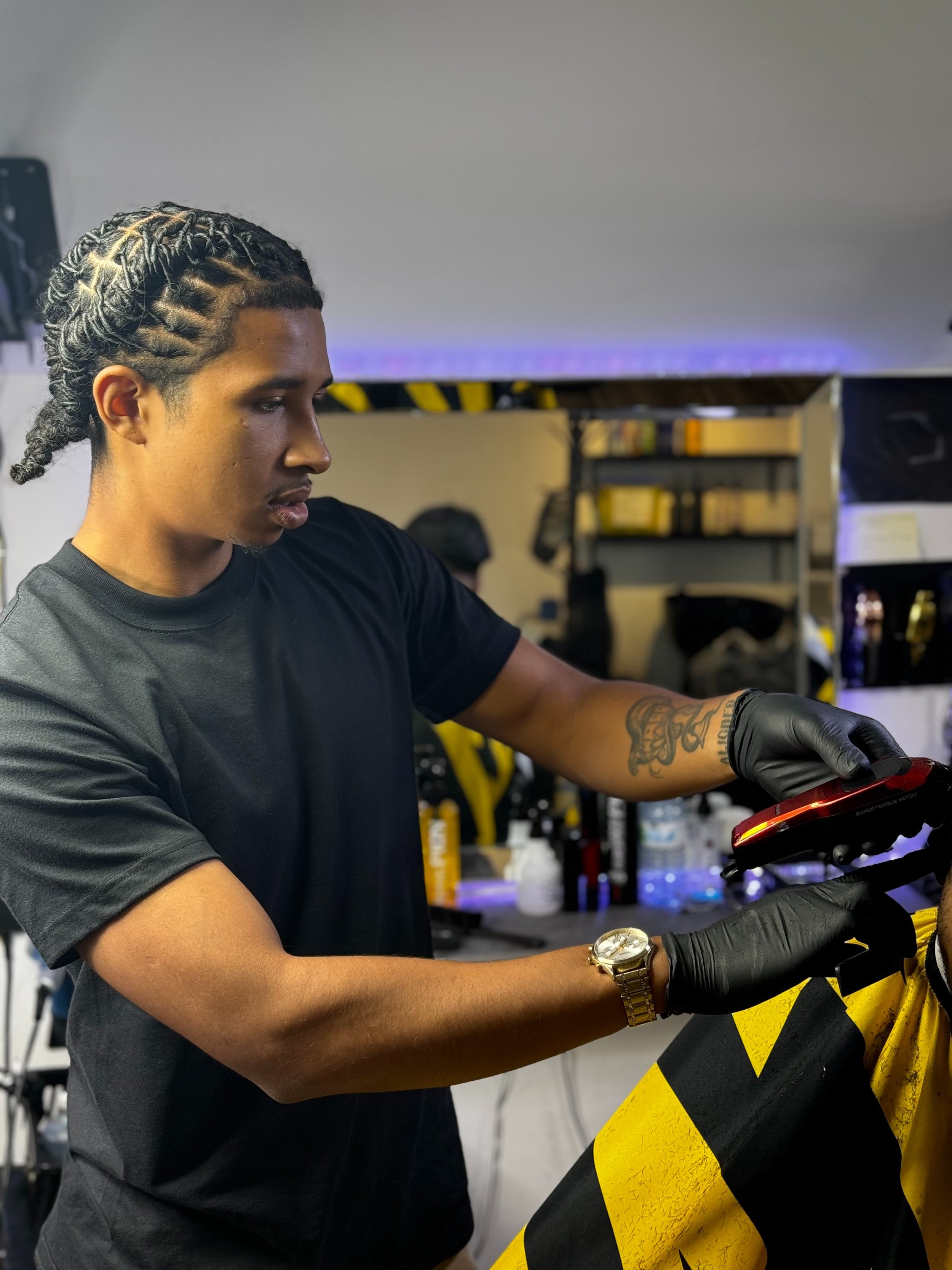 A young man with braided hair wearing black gloves and a gold watch, working on a bicycle in a workshop.