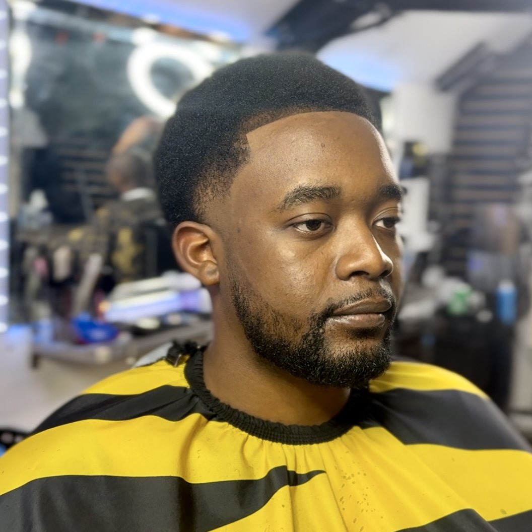 Young man with a fresh haircut in a barbershop wearing a yellow and black barber cape.