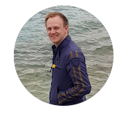 Ein Mann in einer blauen Jacke steht am Wasser.