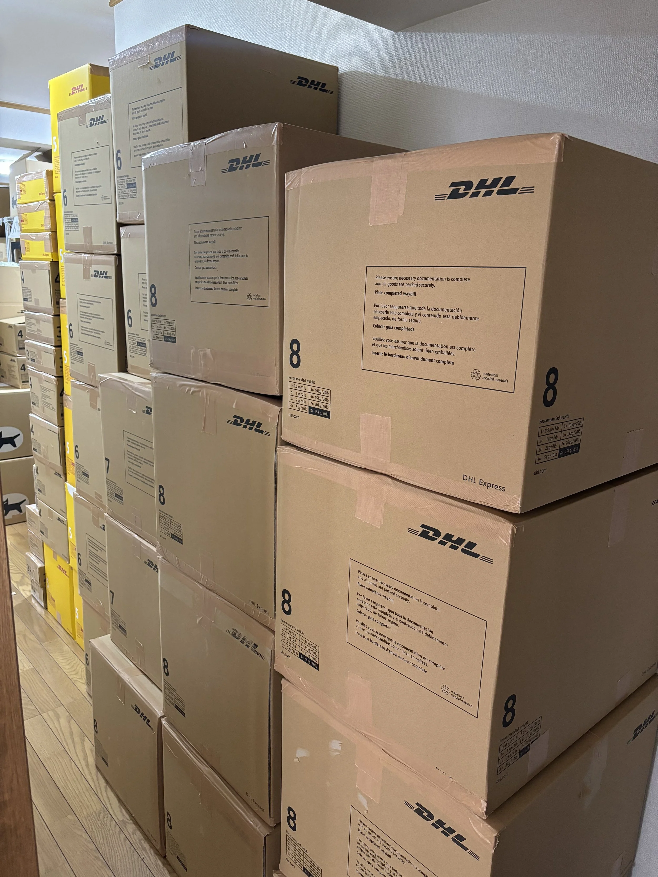 Stack of DHL cardboard boxes in a storage area, some labeled with the number 8, others are yellow boxes labeled 5 and 6.