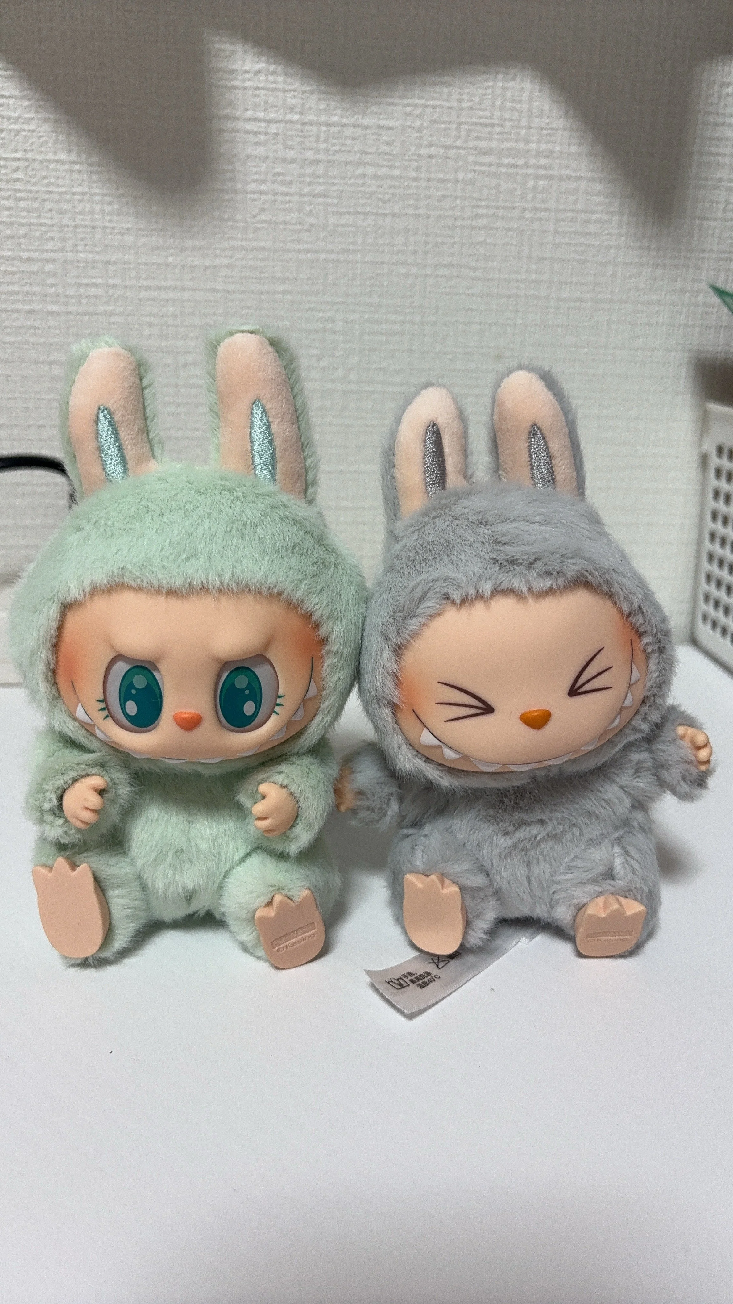 Two plush toys in bunny costumes with furry bodies, large ears, and expressive faces sitting on a white surface.